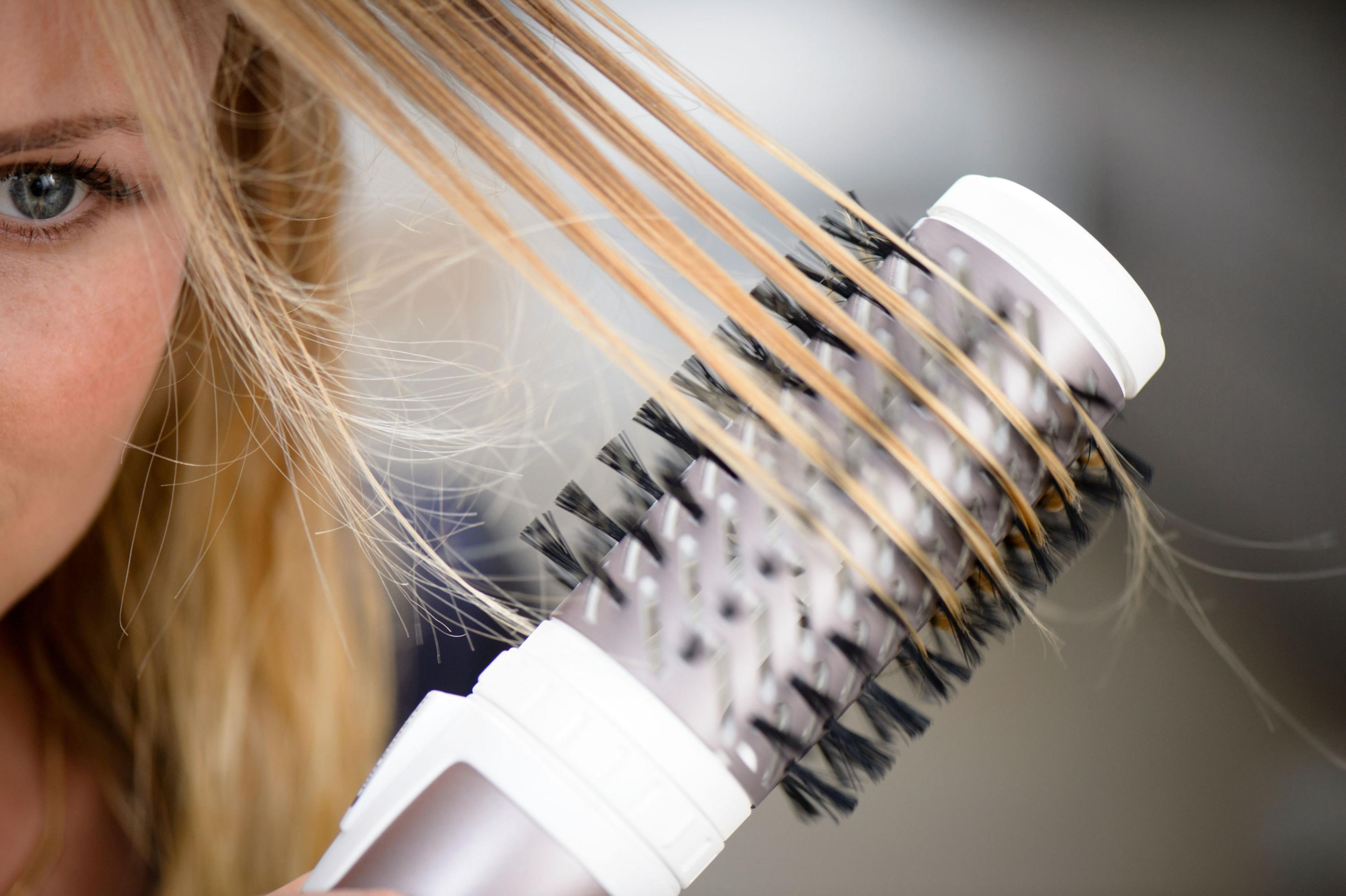 Oko i włosy blondynki, używającej szczotki do suszenia włosów.