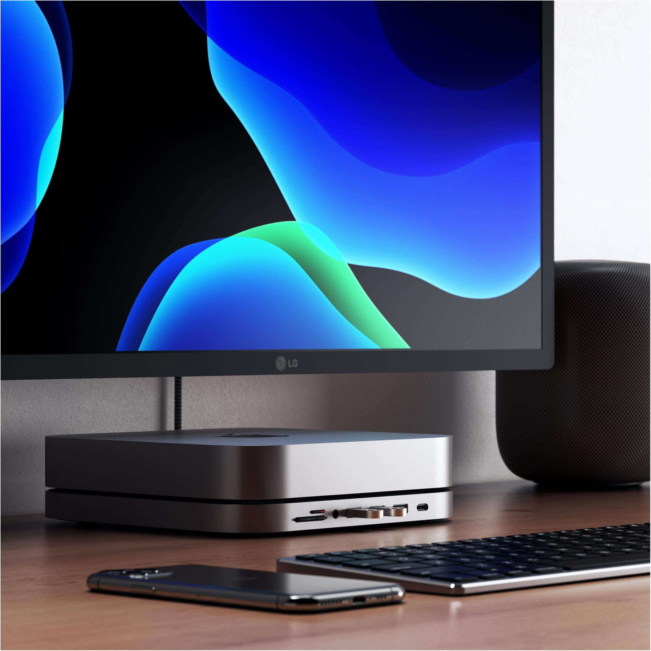 Ein silberner Mac Mini, Monitor mit blau-grünem Hintergrund, schwarze Tastatur und Telefon auf einem Holztisch.