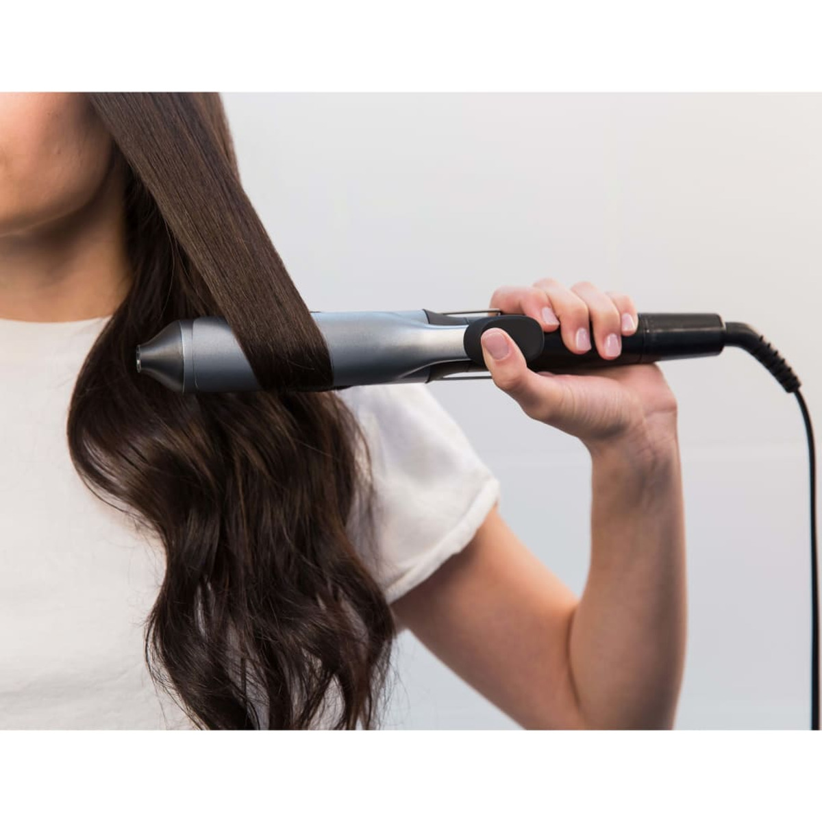 Osoba używająca prostownicy do włosów. Prostownica jest srebrna i czarna.