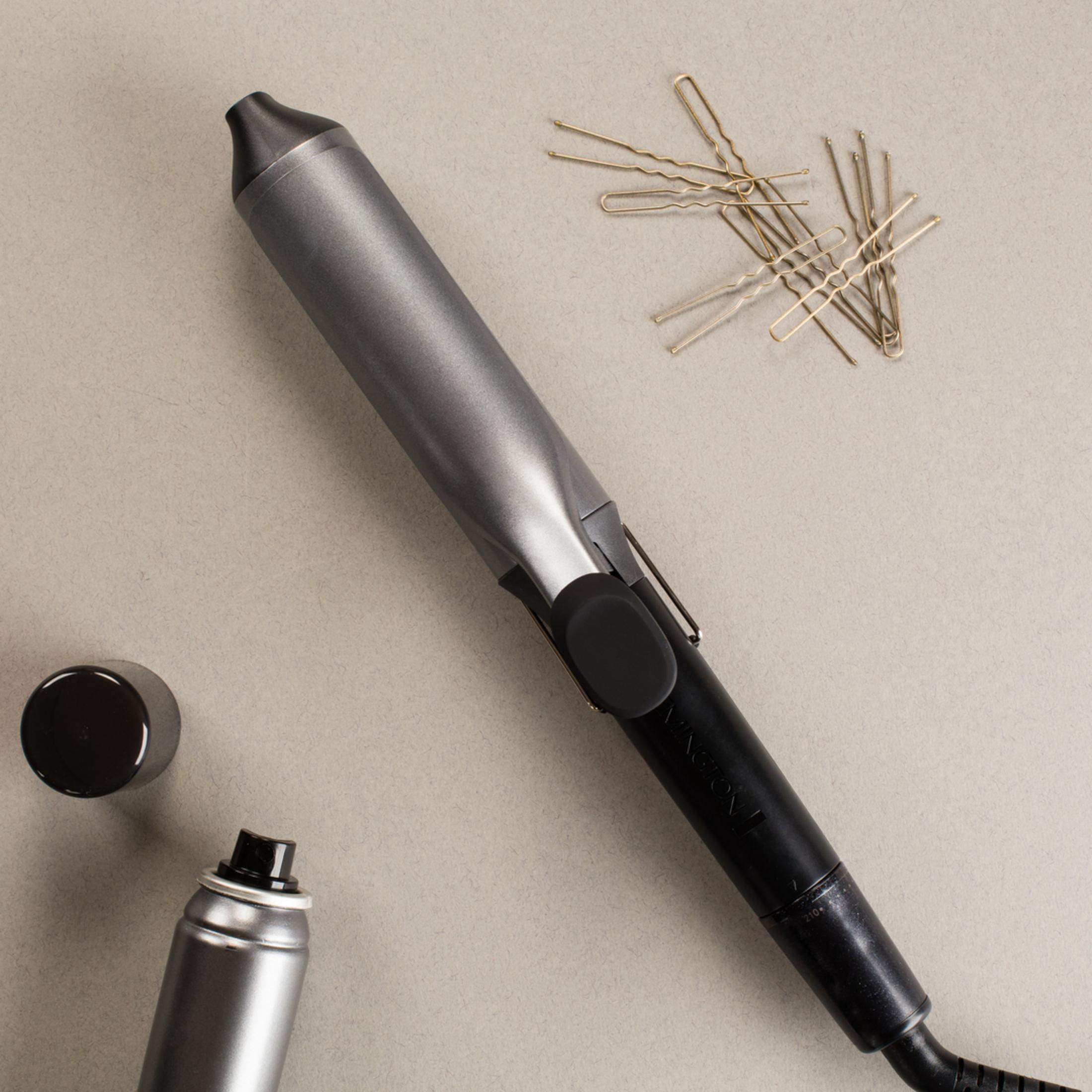 Lokówka do włosów, wsuwki i lakier do włosów na szarej powierzchni. Przedmioty są uporządkowane.