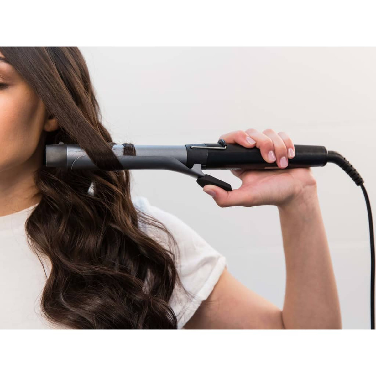 Una donna che si arriccia i capelli con un ferro arricciacapelli argento e nero.