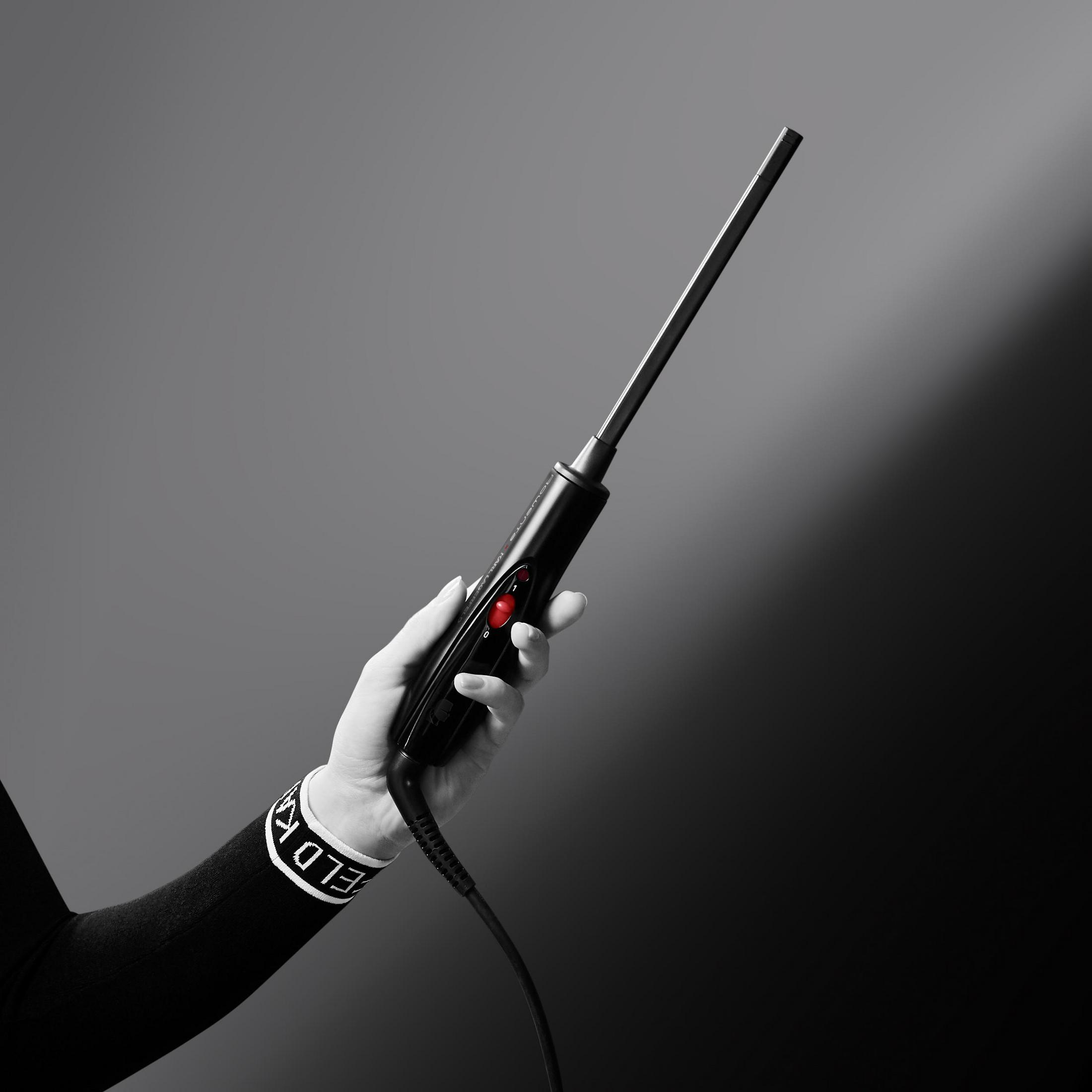 Zbliżenie dłoni trzymającej czarną lokówkę z czerwonym przyciskiem zasilania.