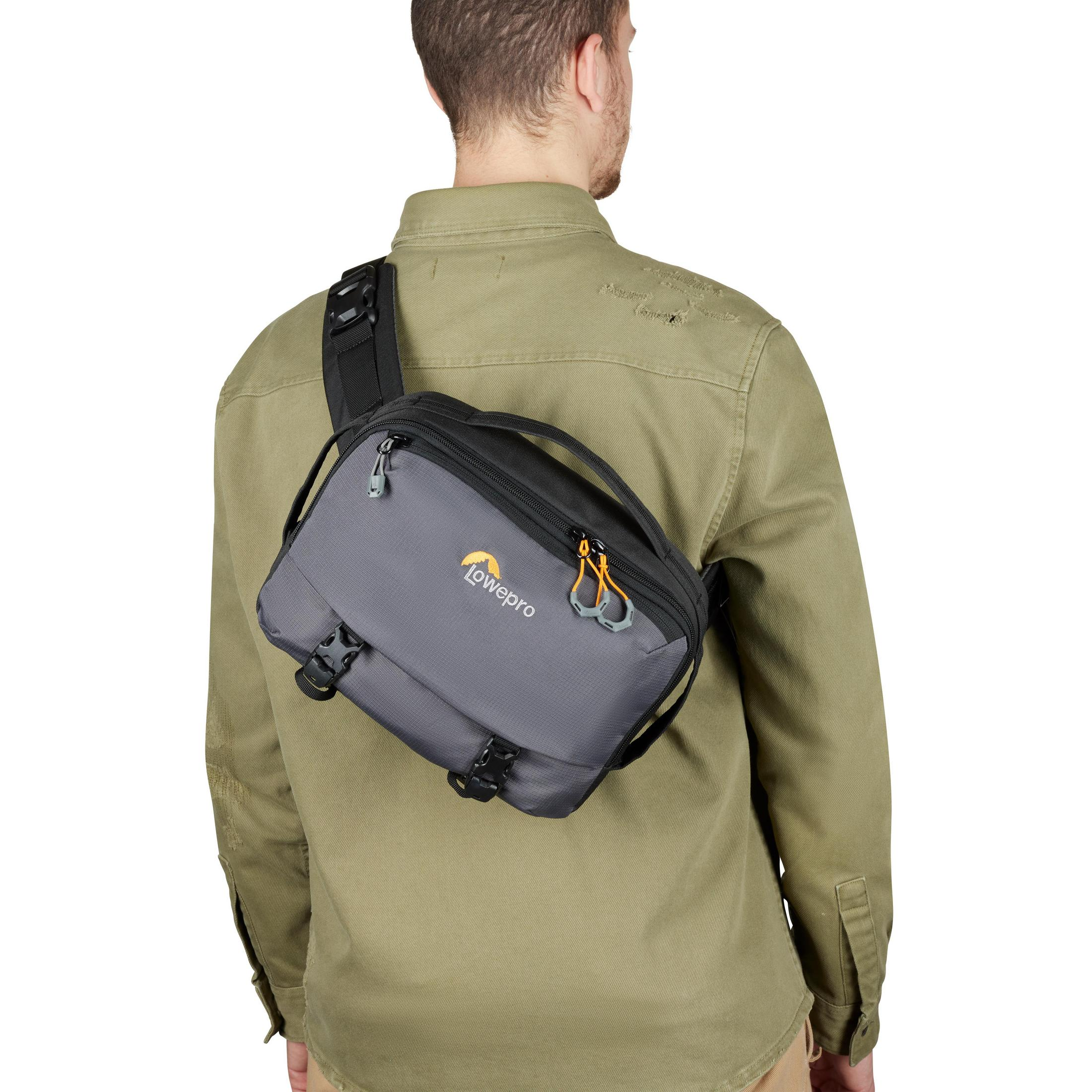 Persona vista da dietro con borsa fotocamera grigia sulla spalla. La borsa ha un logo. Camicia verde.