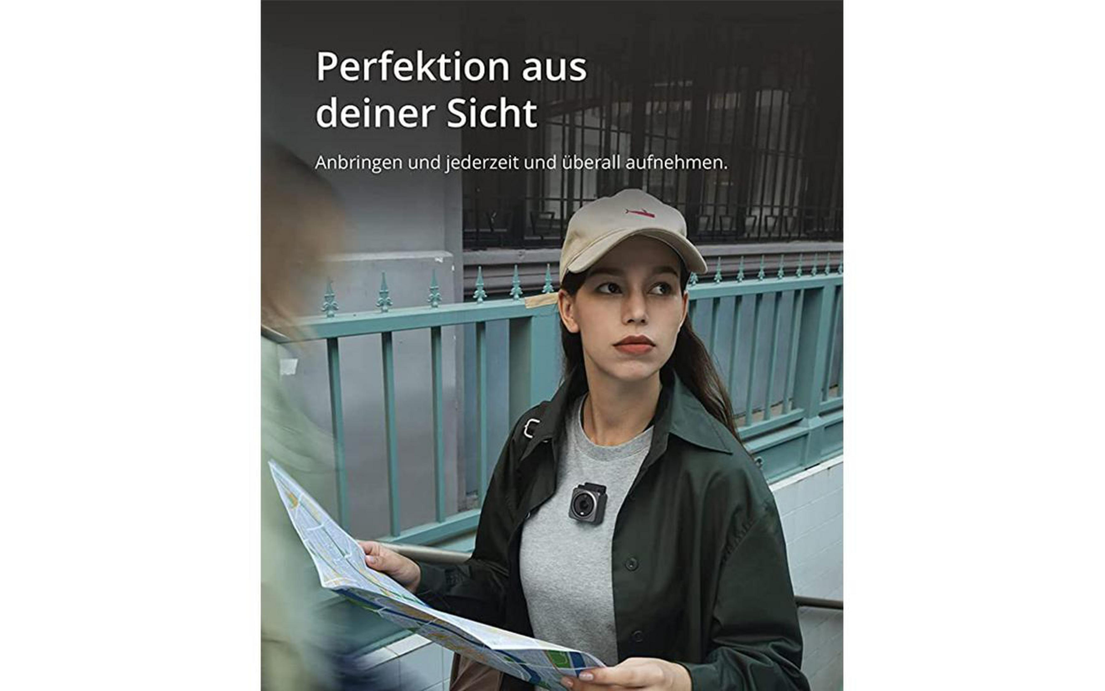 Eine Frau mit Mütze und grüner Jacke hält eine Karte und eine Kamera an ihrem Hemd.