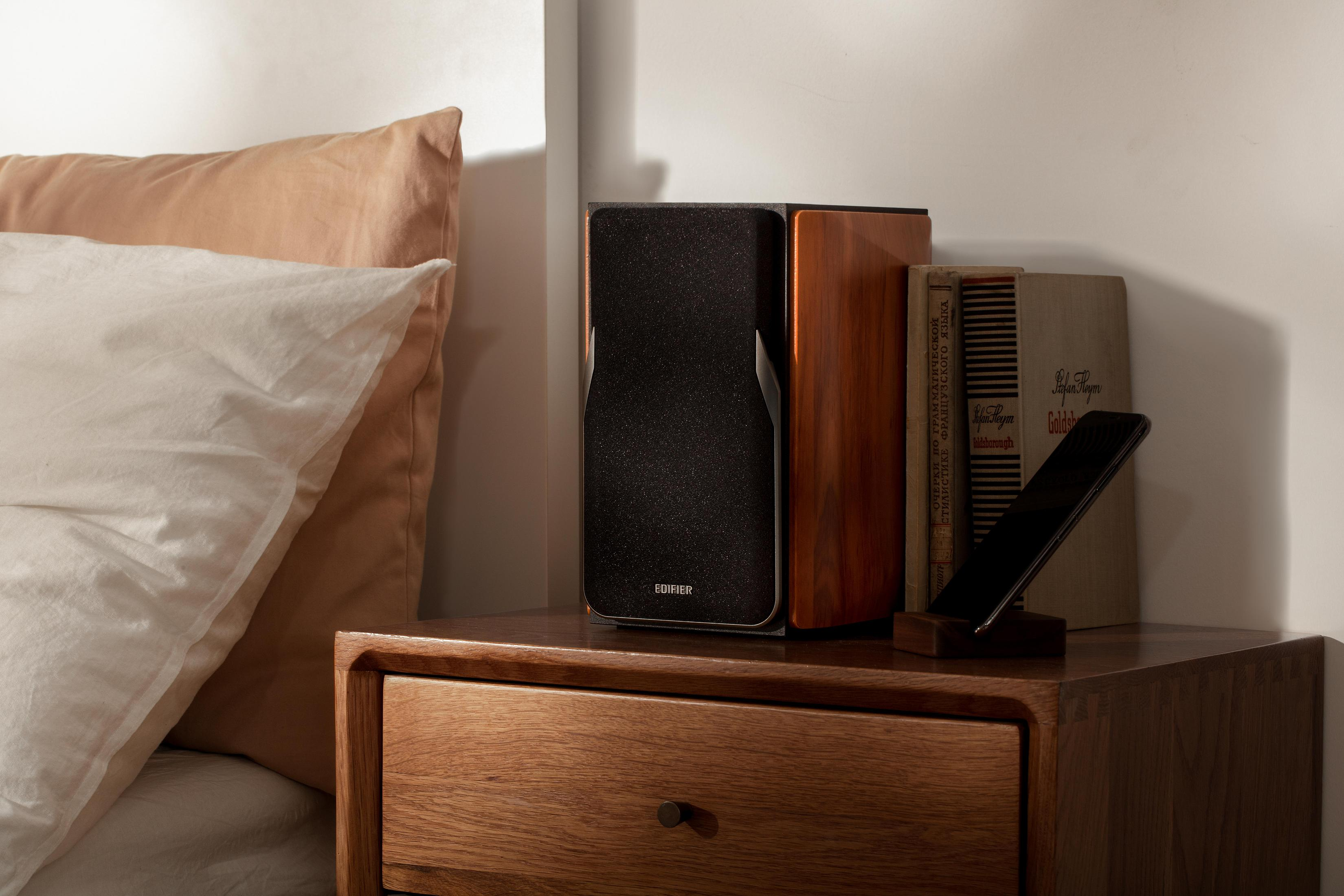 Altoparlanti, libri e un telefono su un comodino. Sono visibili anche un cuscino e una coperta.