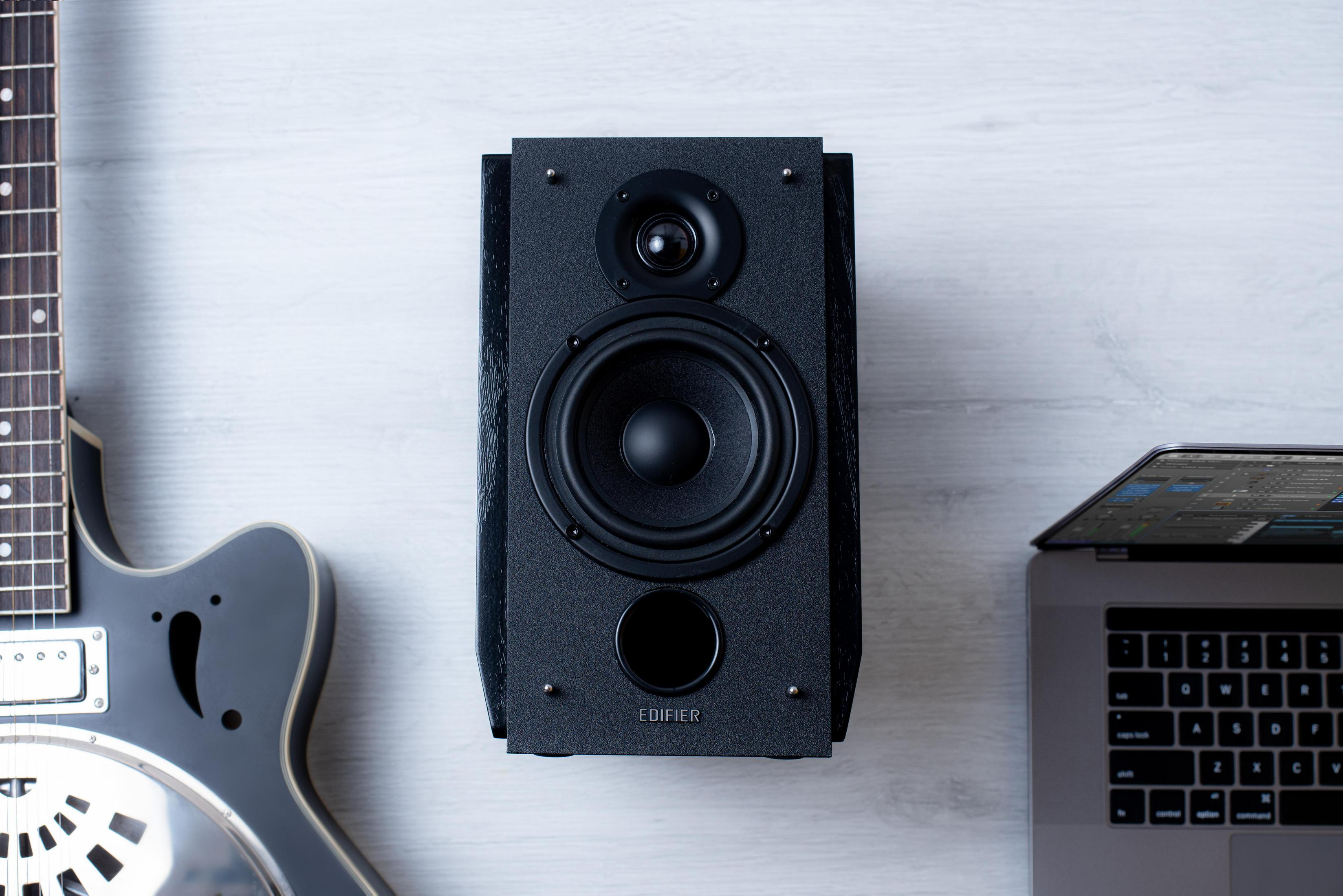 Czarny głośnik na białej powierzchni z widoczną gitarą i laptopem.