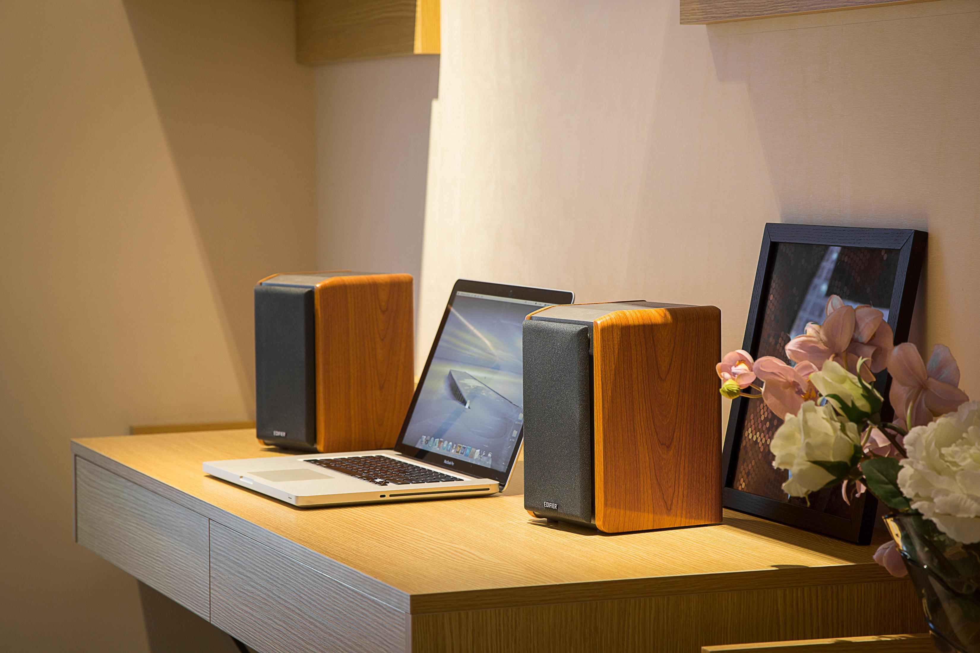 Zwei Holz-Lautsprecher, ein Laptop und ein Bilderrahmen auf einem Schreibtisch. Hintergrund: eine Wand.