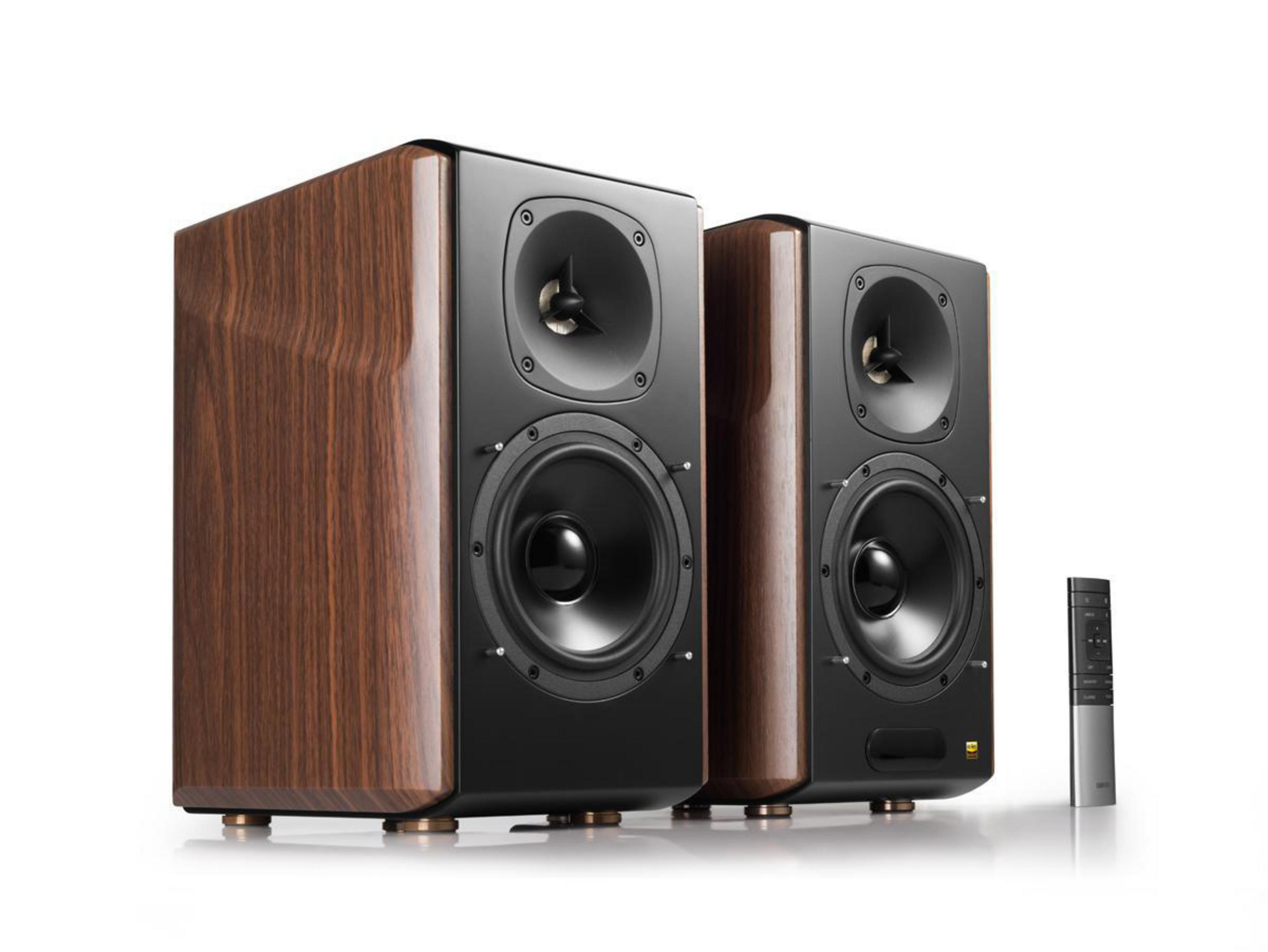 Dwa głośniki z fakturą drewna, czarne przody. Pilot po prawej. Białe tło.