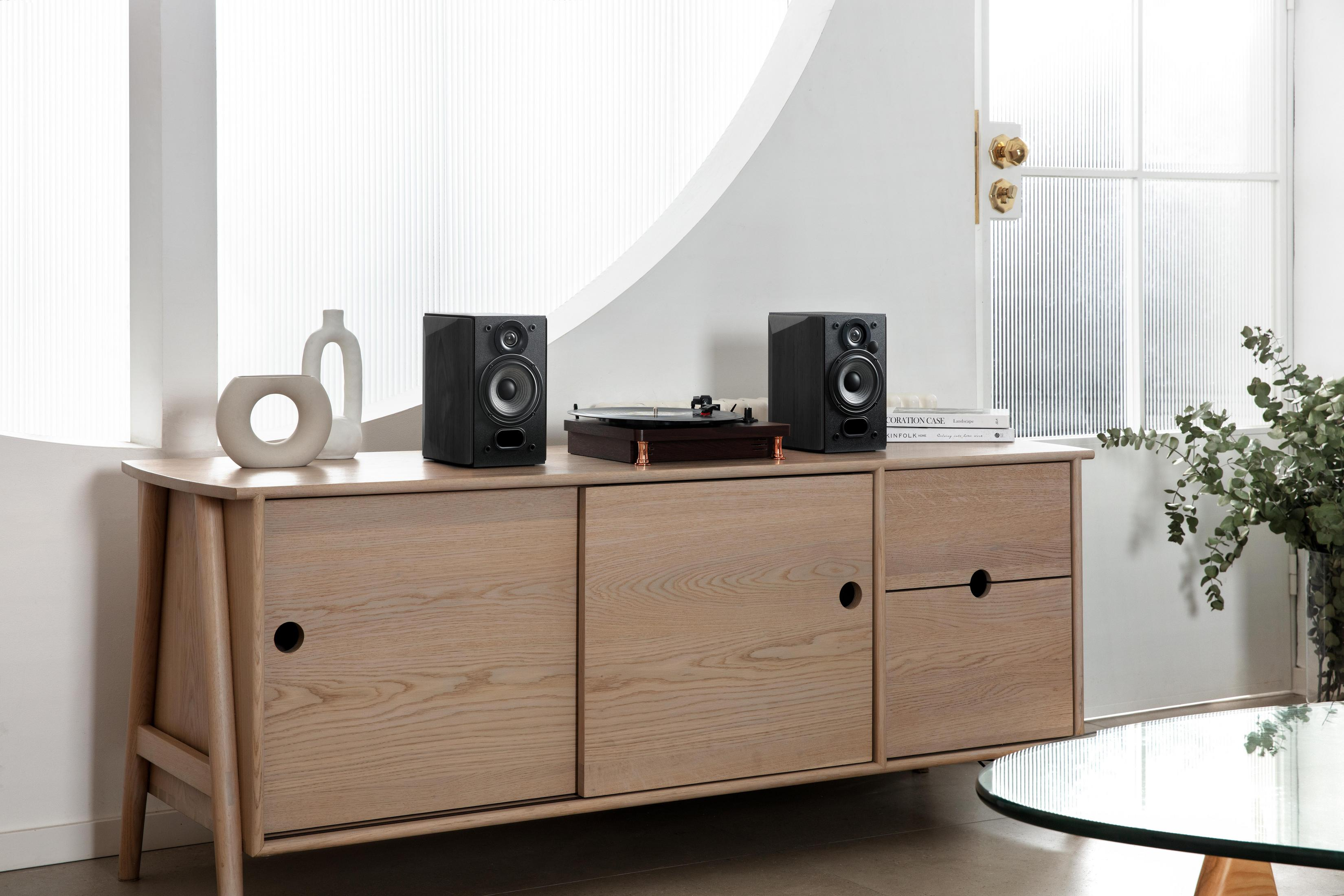 Due altoparlanti neri, giradischi e oggetti decorativi su un mobile in legno.