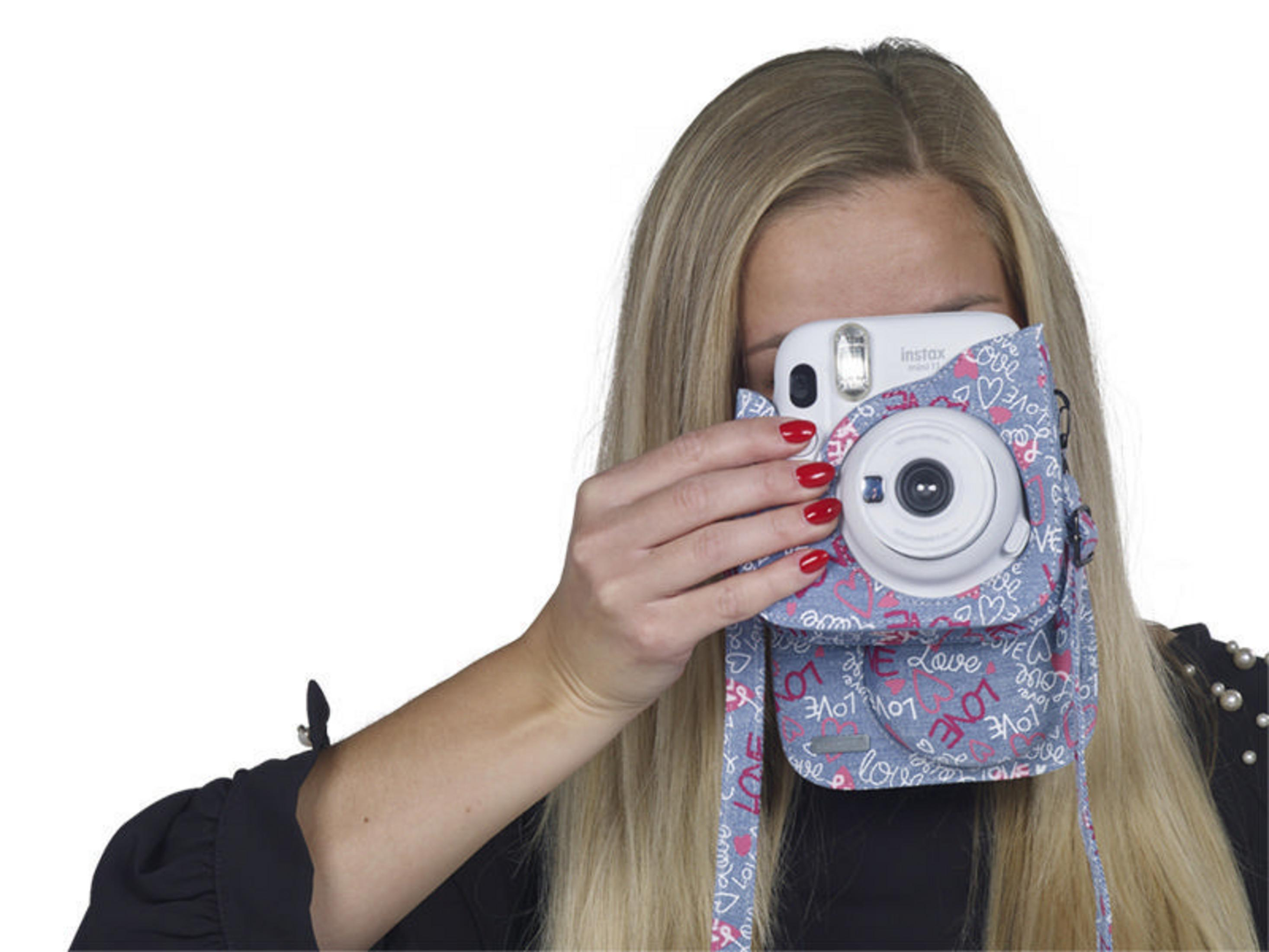 Blonde Frau hält eine weiße Instax-Kamera mit bedrucktem Gehäuse. Weißer Hintergrund.