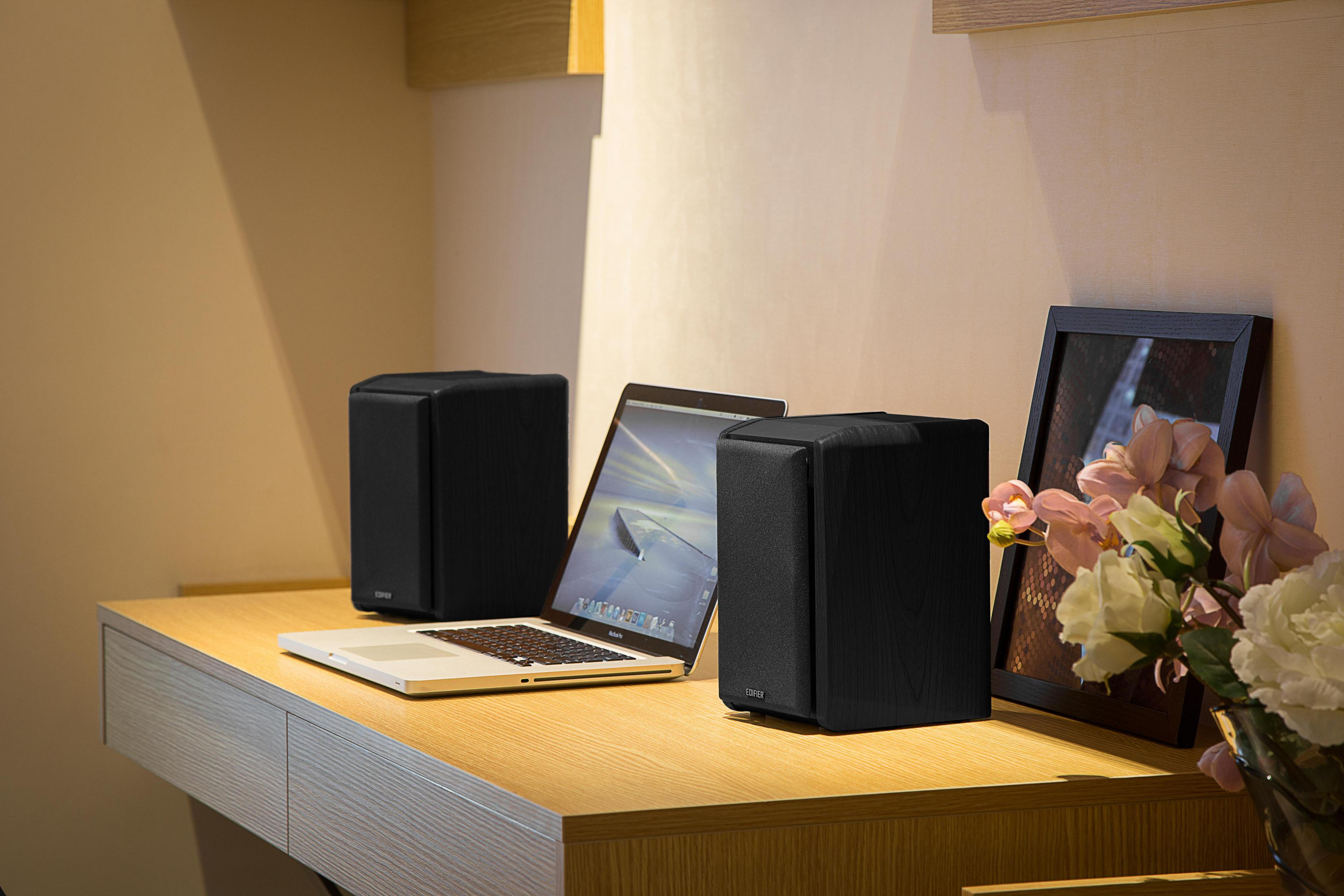 Dwa czarne głośniki, laptop i oprawione zdjęcie na drewnianym biurku.