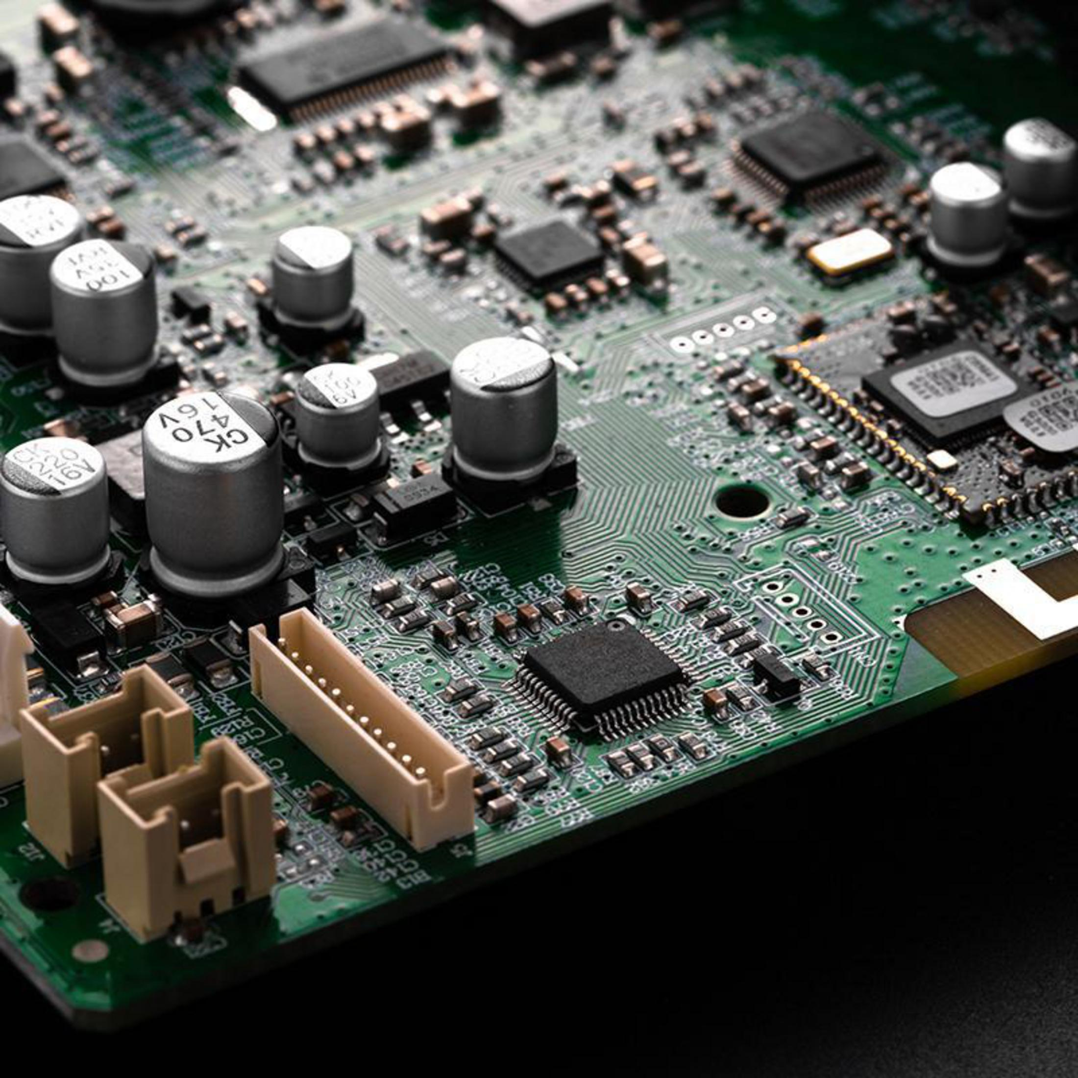 Primo piano di un circuito stampato verde con componenti elettronici. Ha chip, condensatori e connettori.