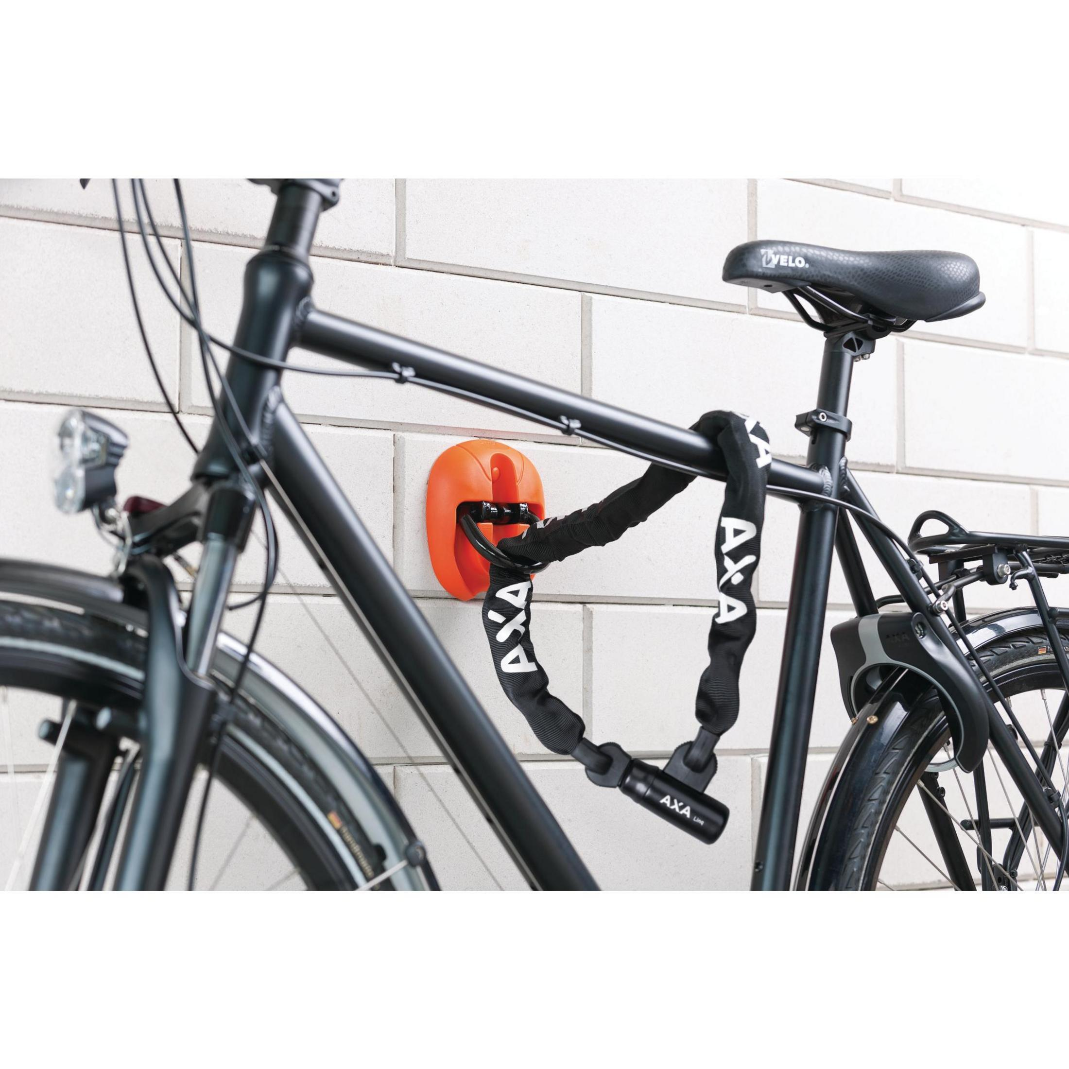 Schwarzes Fahrrad mit Kettenschloss an einer orangefarbenen Wandhalterung befestigt.