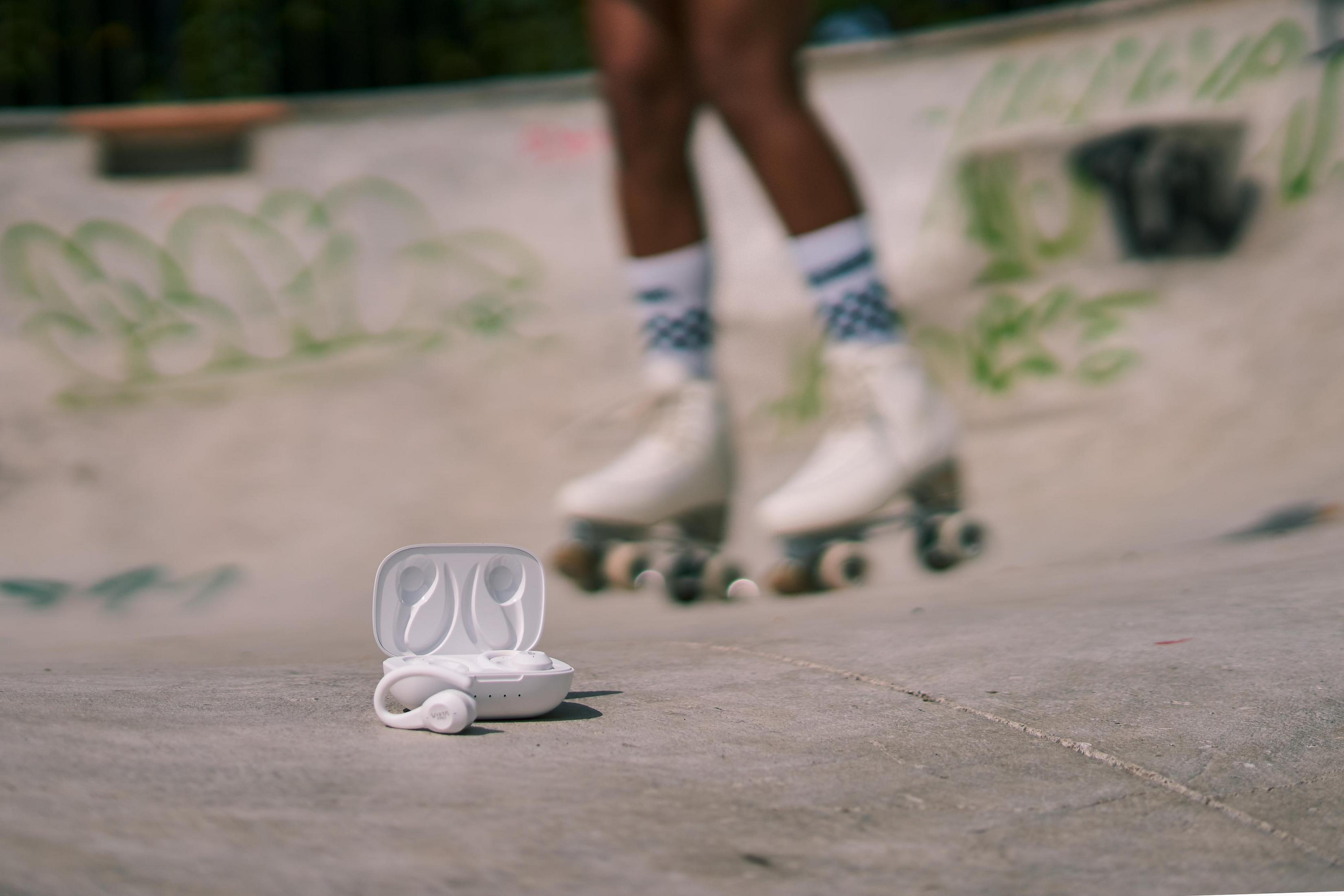 Weiße kabellose Ohrhörer im Etui auf Beton. Skater im Hintergrund. Skateboard-Park.