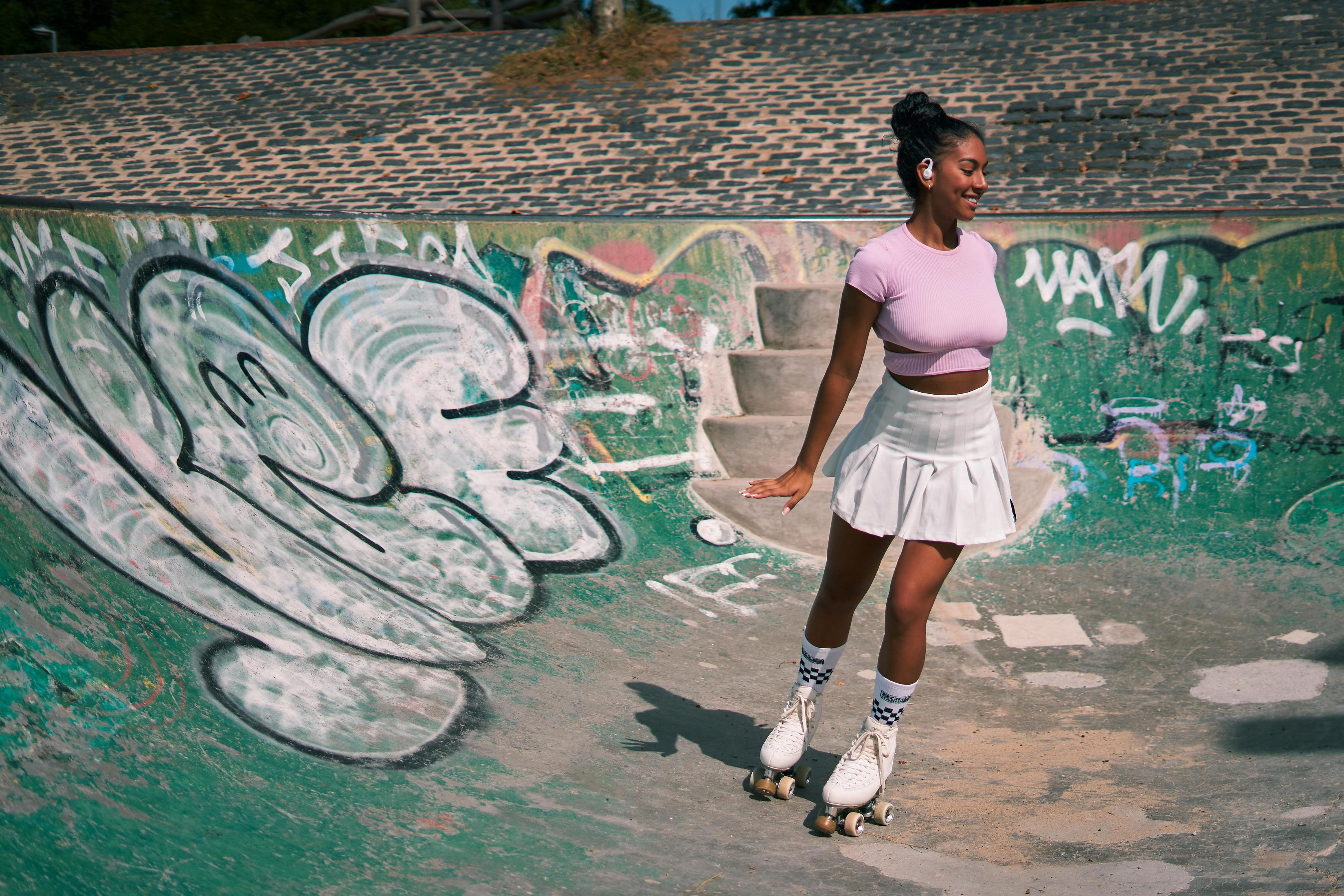 Frau fährt im Skatepark Rollschuh. Graffiti an den Wänden.