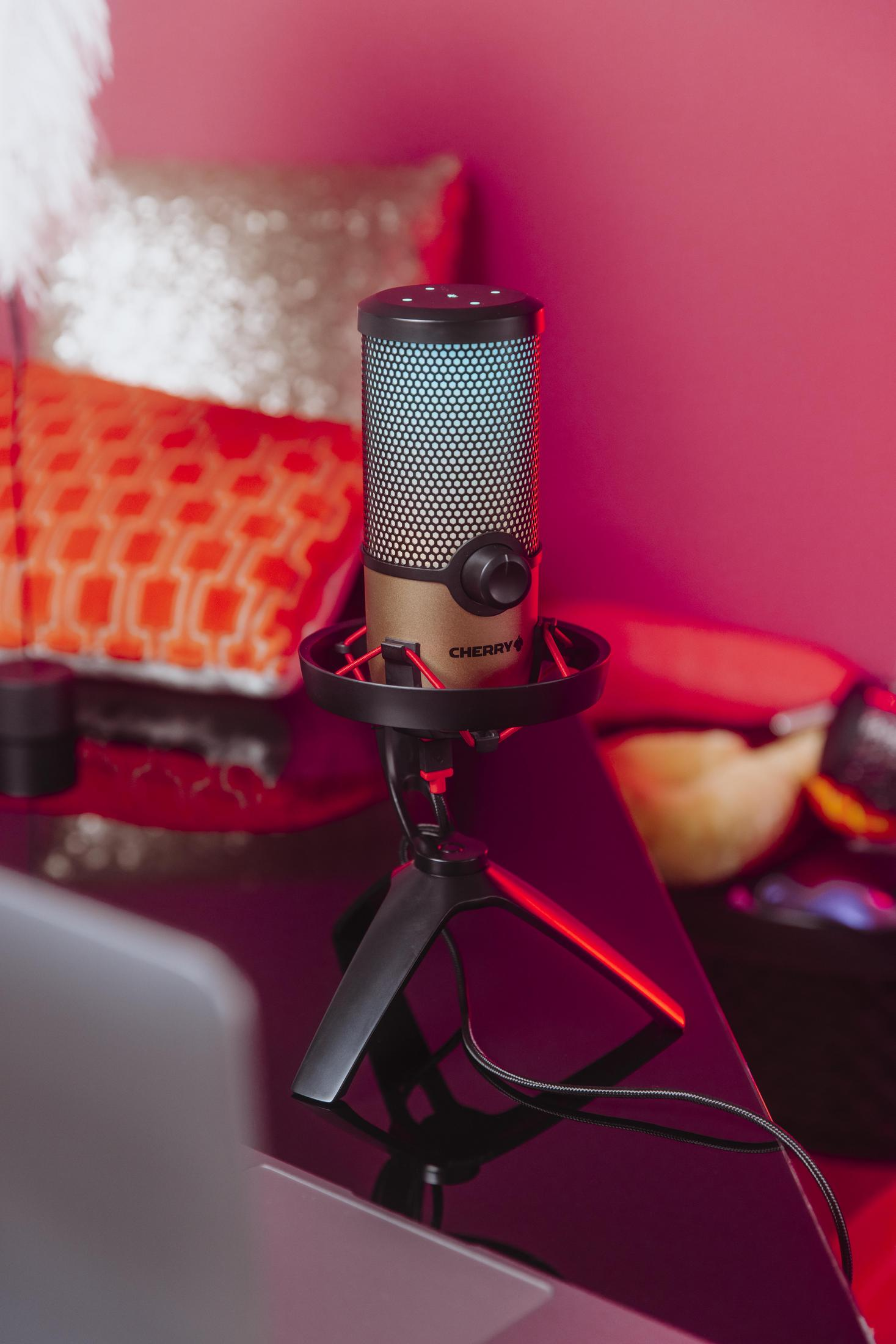 Black microphone on a stand. Gold body, black base. Red light. Pink background.
