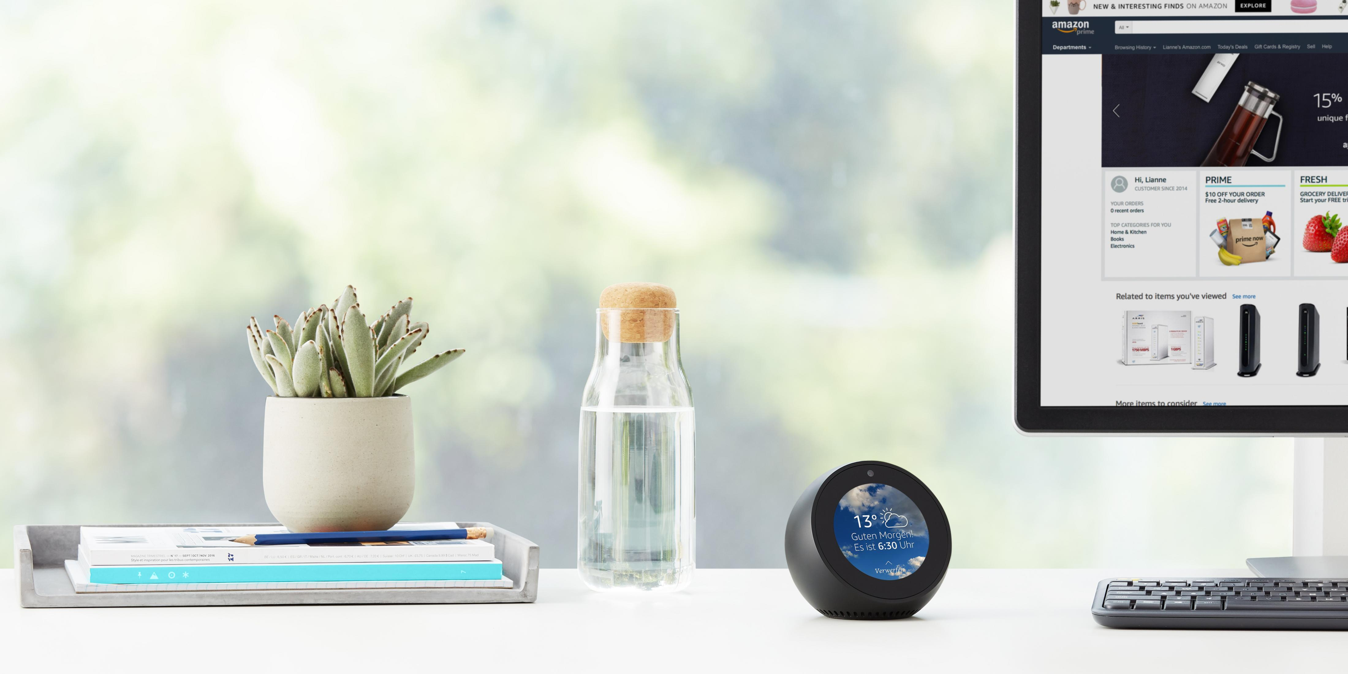 Bürotischszene mit einem intelligenten Lautsprecher, Pflanze, Wasserflasche und Computer mit Amazon-Website.