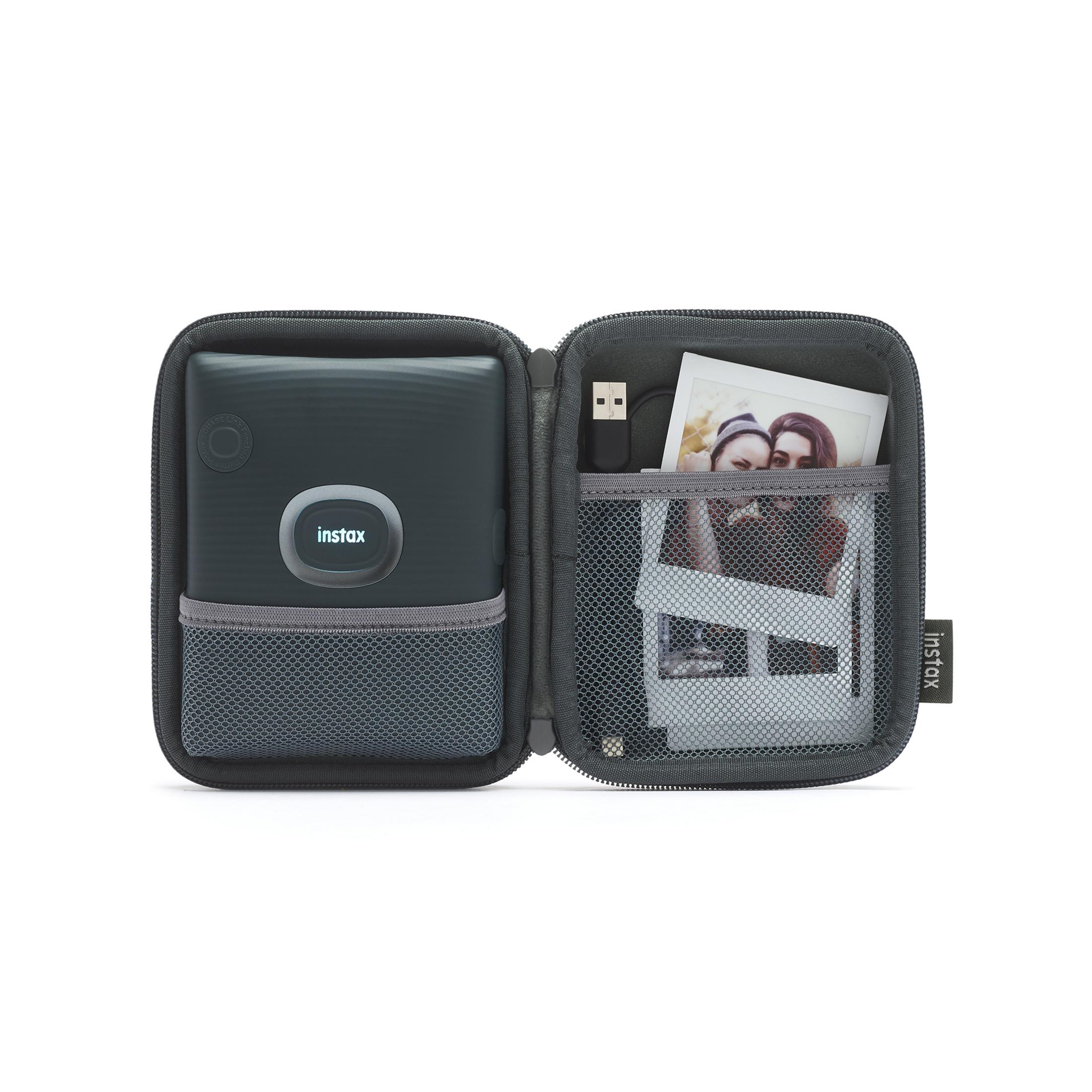 Instax graue Hülle, geöffnet, mit Instax Kamera, Kabel und Fotoabzug, auf weißem Hintergrund.
