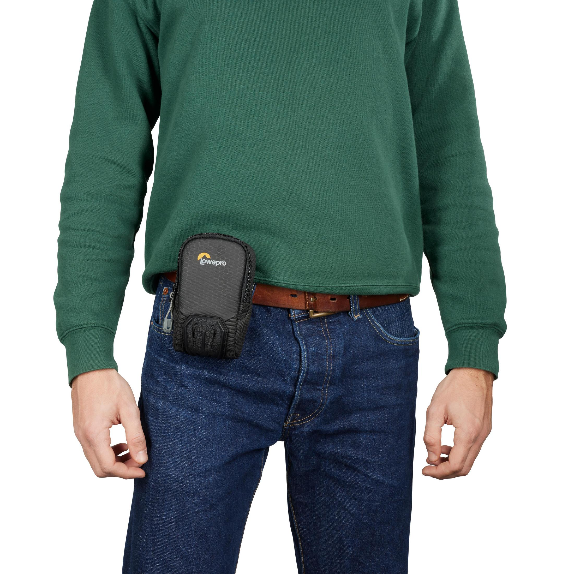 Ein Mann mit grünem Pullover und blauer Jeans hat eine schwarze Tasche um die Hüfte.