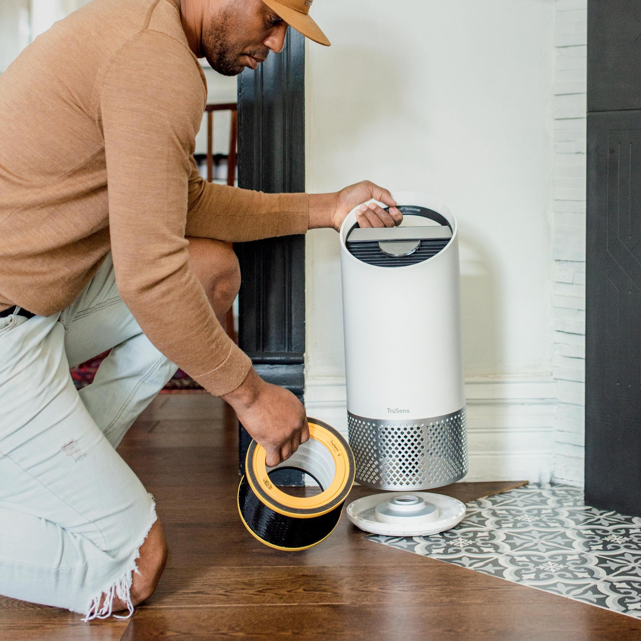 Mężczyzna instaluje filtr powietrza w białym oczyszczaczu powietrza.