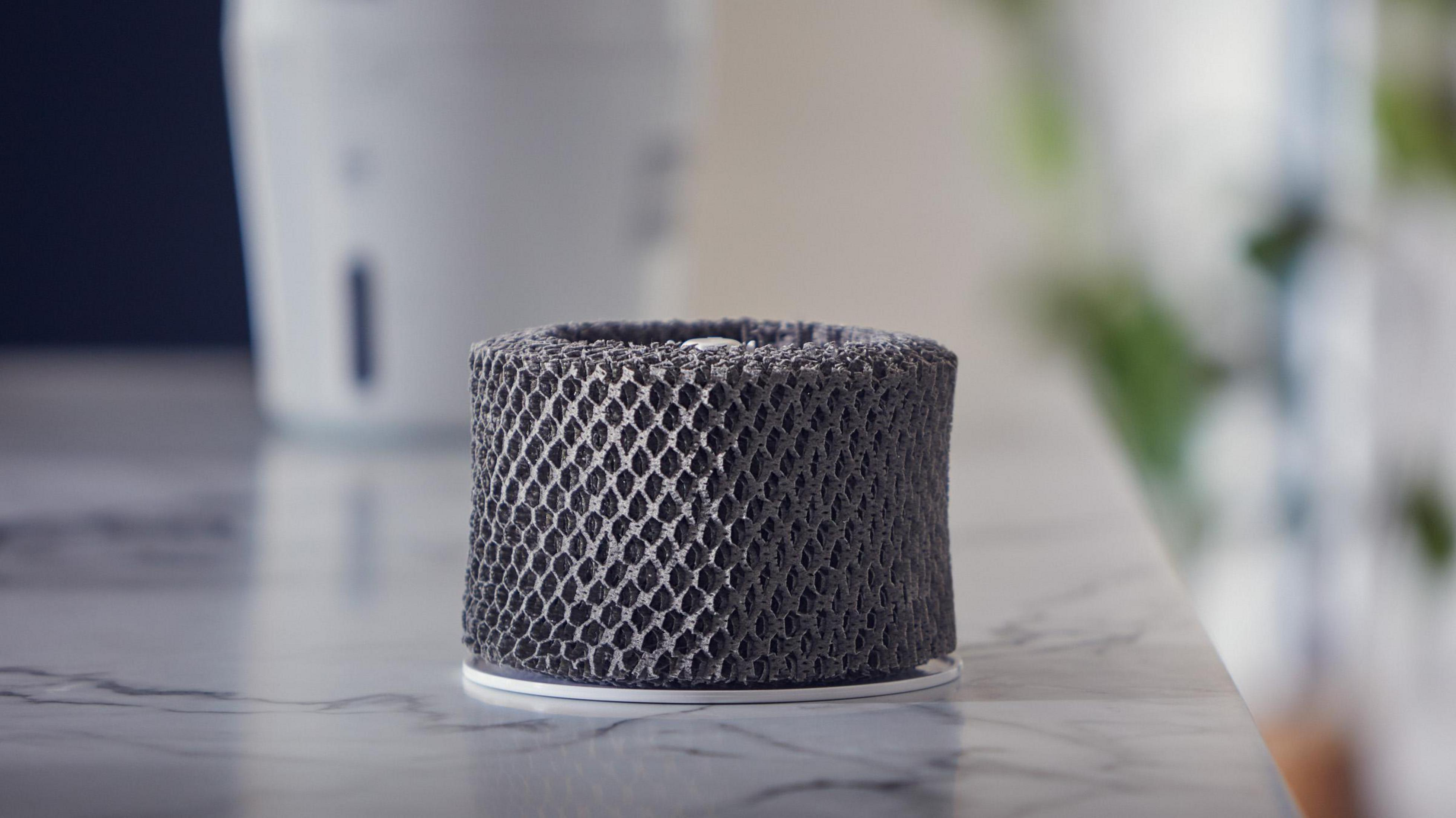 Zbliżenie cylindrycznego szarego filtra powietrza z wzorem plastra miodu. Leży na marmurowej powierzchni.