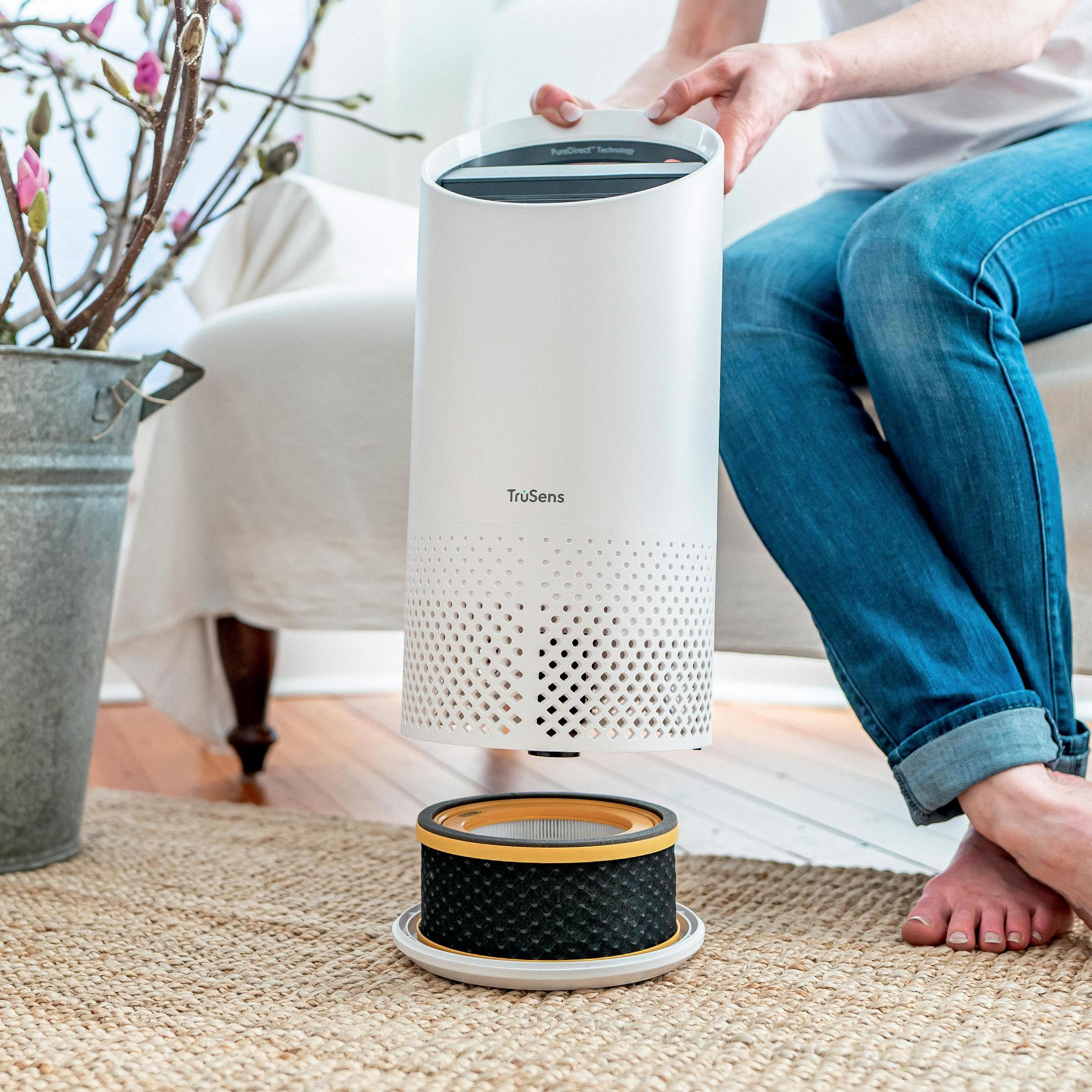 Kobieta wyjmuje filtr z białego oczyszczacza powietrza. Filtr i dywan na pierwszym planie.