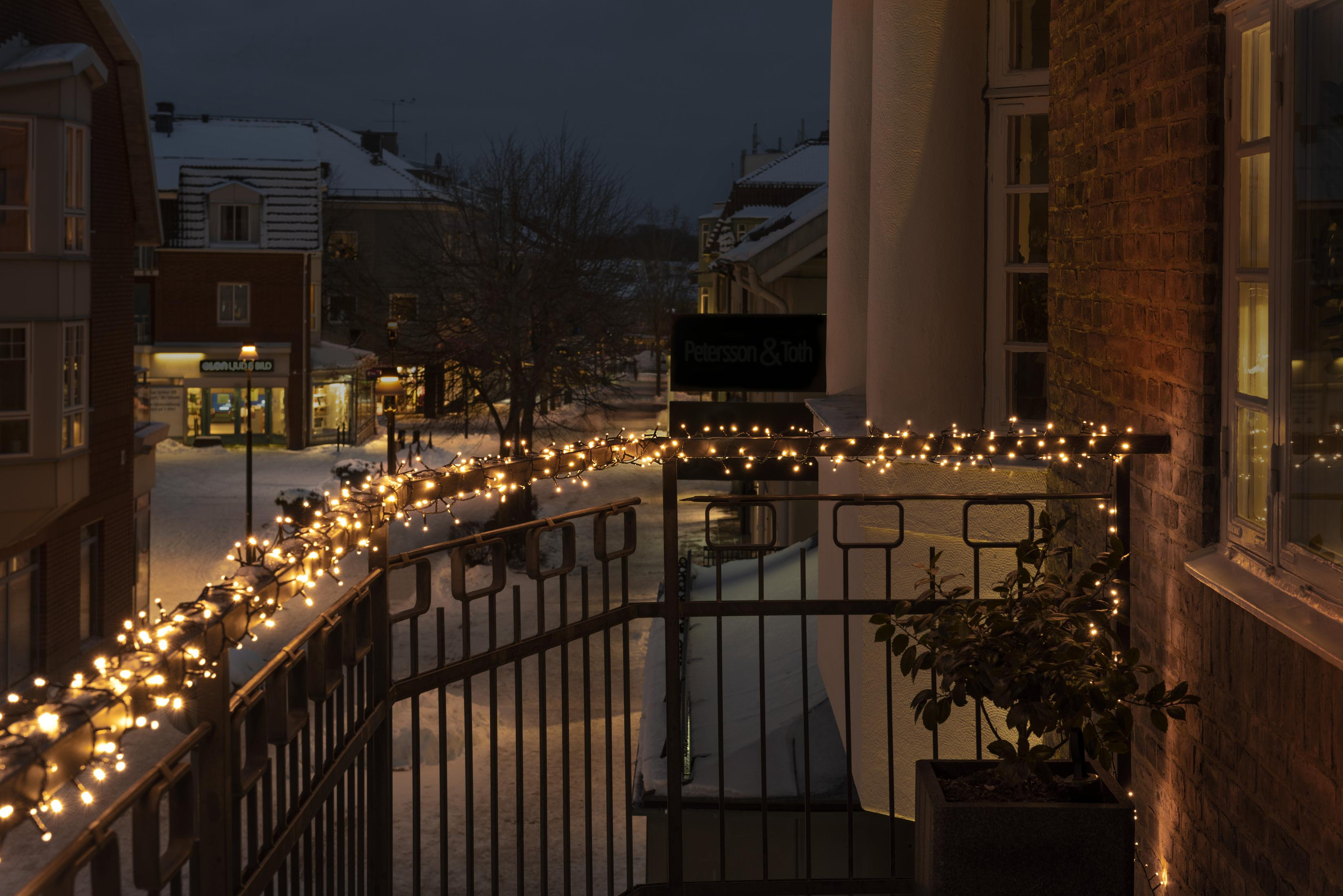 Balkon mit Lichterketten. Eine Straßenszene mit Schnee auf den Bürgersteigen bei Nacht.
