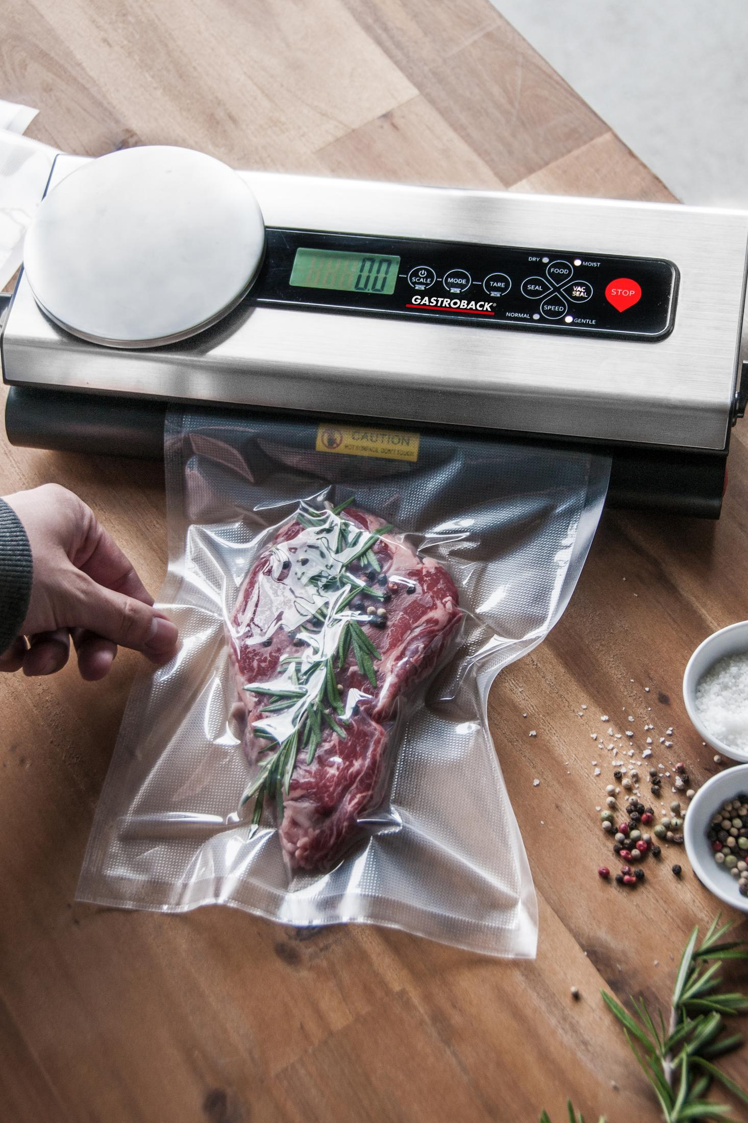 Ein Steak in einem Plastikbeutel, das von einer silber-schwarzen Maschine auf einer Holzoberfläche vakuumiert wird.