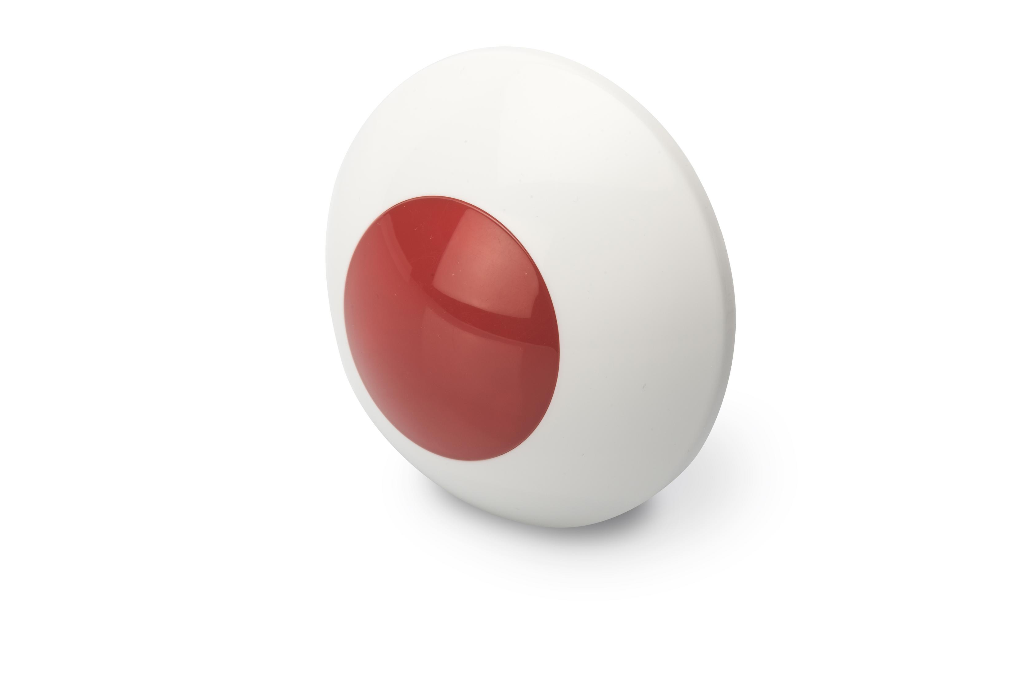 Un objeto blanco y rojo, posiblemente un botón, con un círculo rojo sobre una superficie blanca.