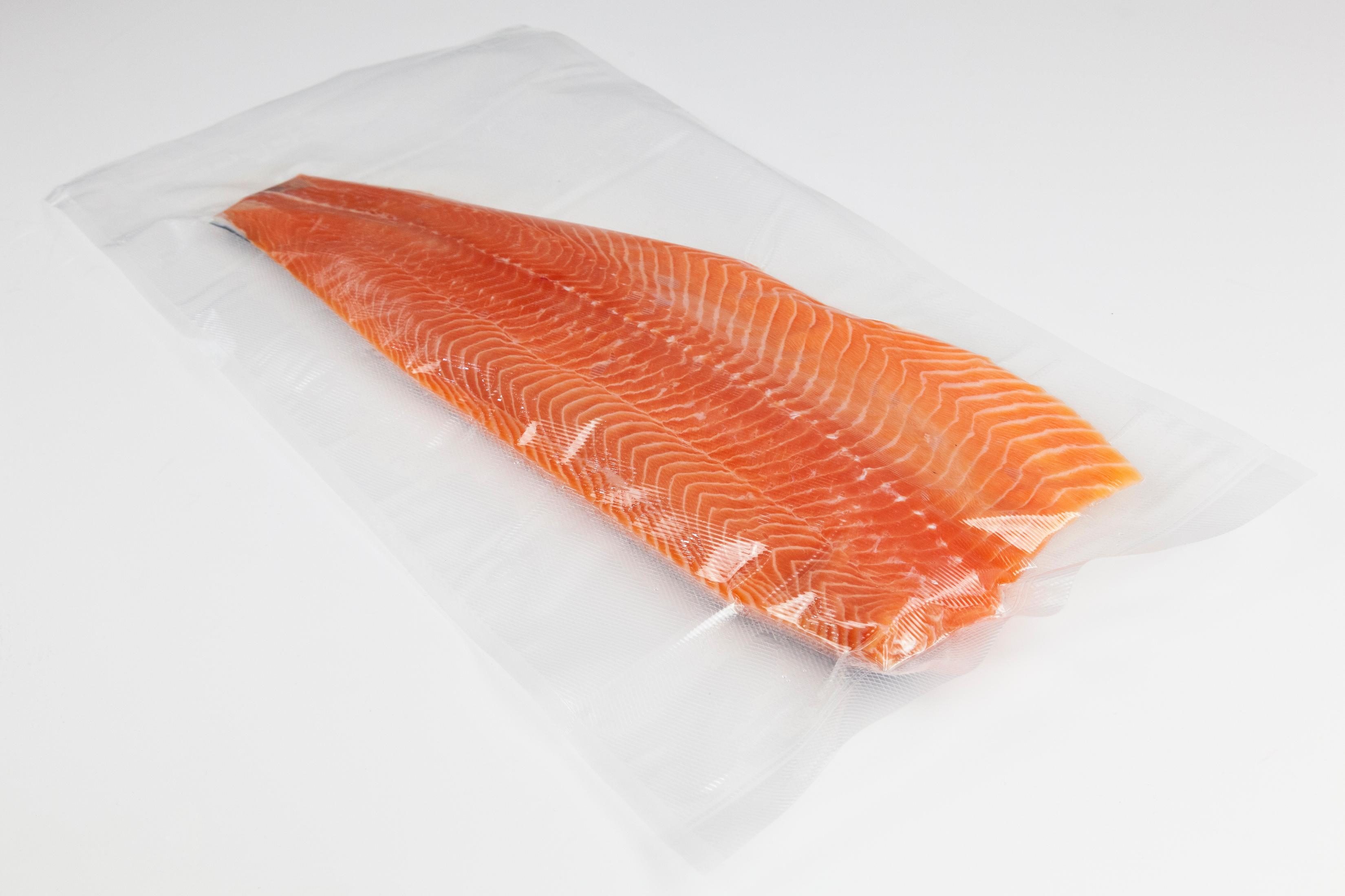 Lachsfilet in einer durchsichtigen Plastiktüte. Der Lachs ist orange mit weißen Linien. Weißer Hintergrund.