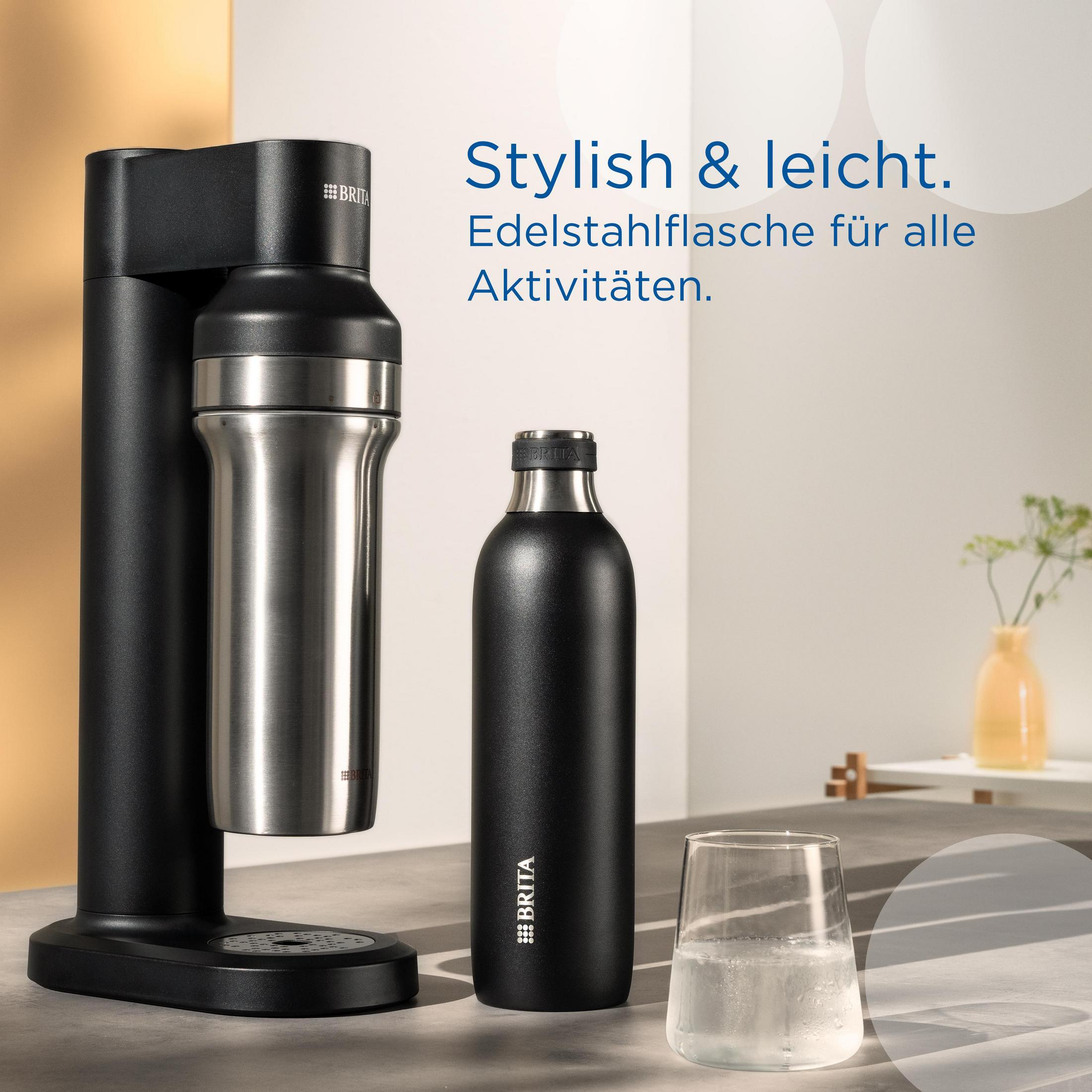 Ein schwarzer Sodabereiter, eine Edelstahlflasche und ein Glas mit Wasser.
