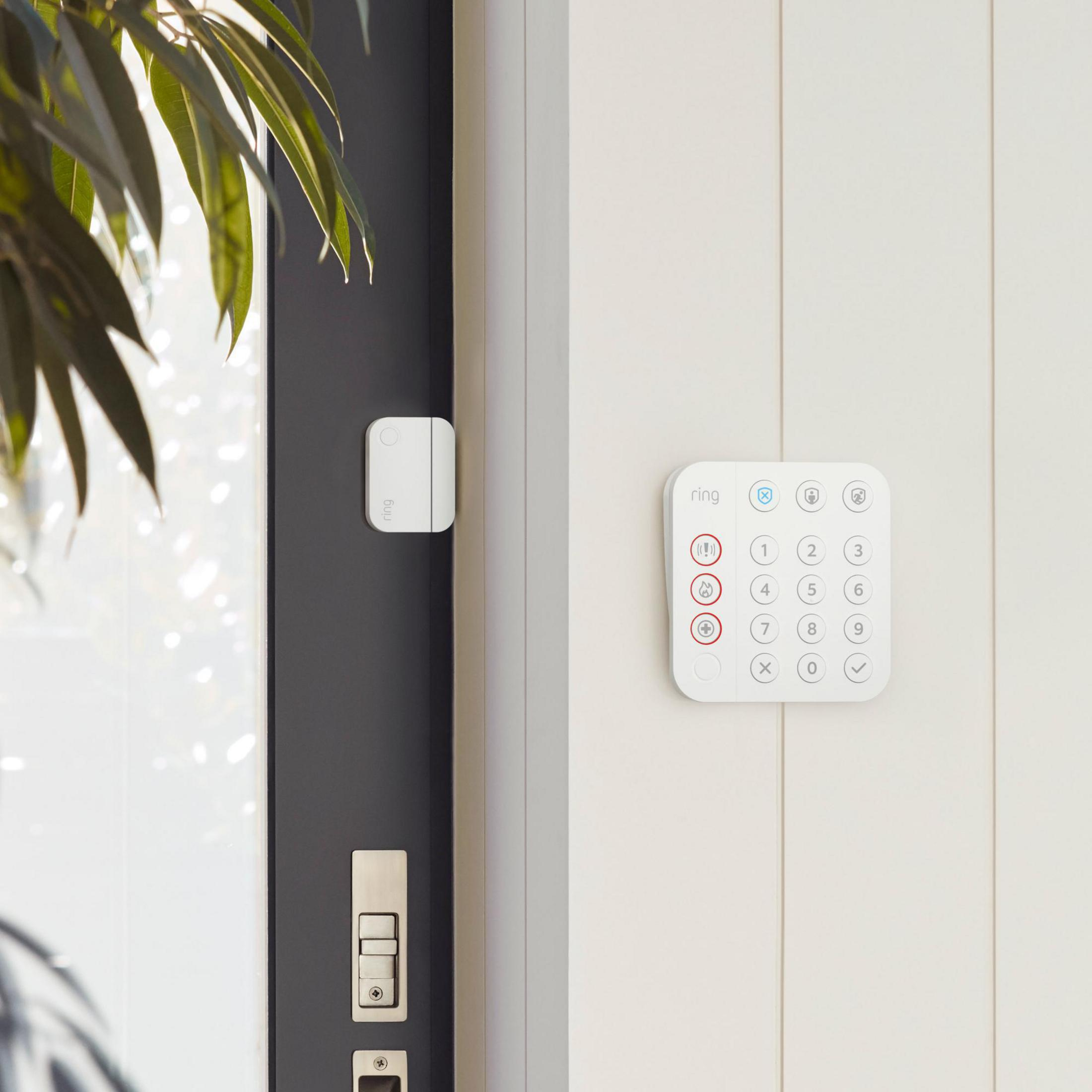 Weißes Ring-Sicherheitssystem-Tastenfeld und Sensor an einer weißen Wand neben einer Tür.