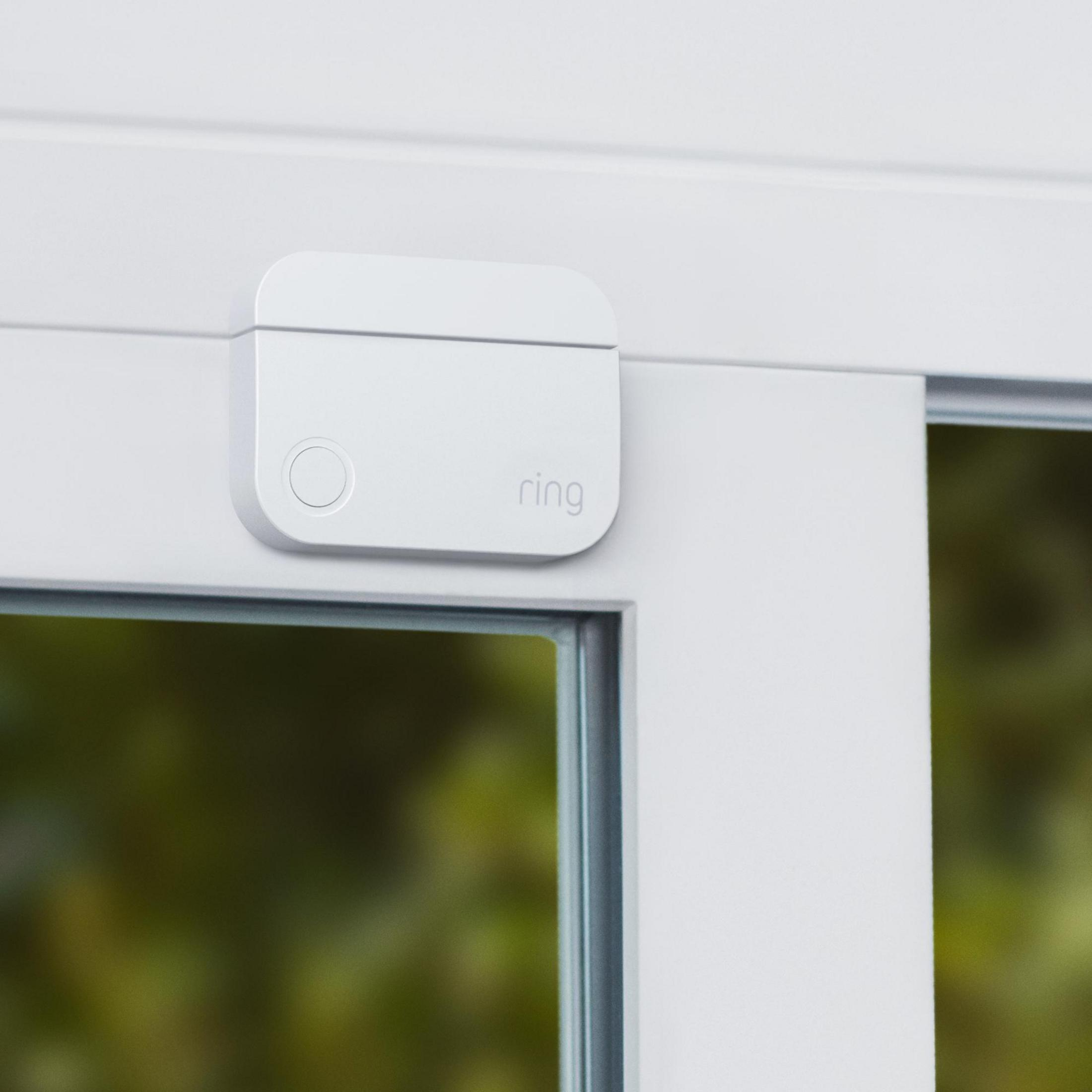 Weißer Ring-Sicherheitssensor an einem weißen Rahmen, in der Nähe eines Fensters. Das Ring-Logo ist sichtbar.