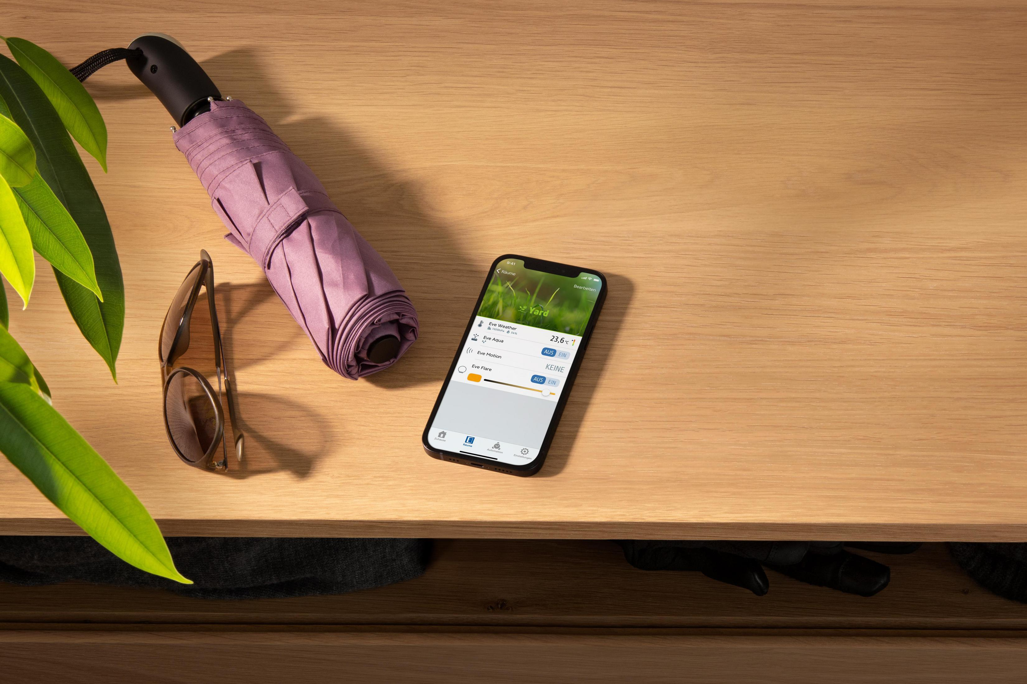 Ein Holztisch mit einem Regenschirm, einer Sonnenbrille und einem App-anzeigenden Telefon.