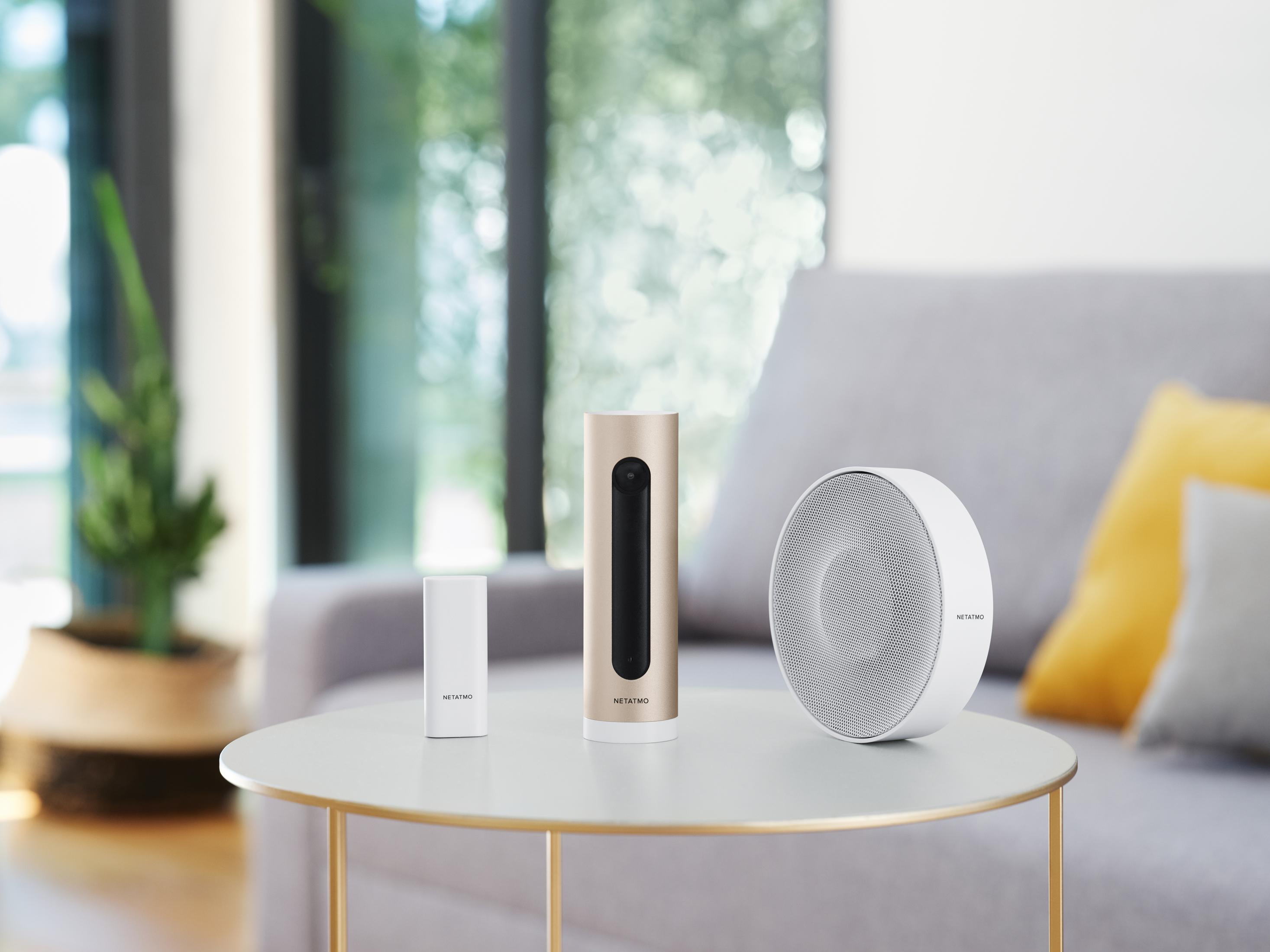 Tre dispositivi Netatmo su un tavolo: sensore bianco, fotocamera dorata, altoparlante bianco.
