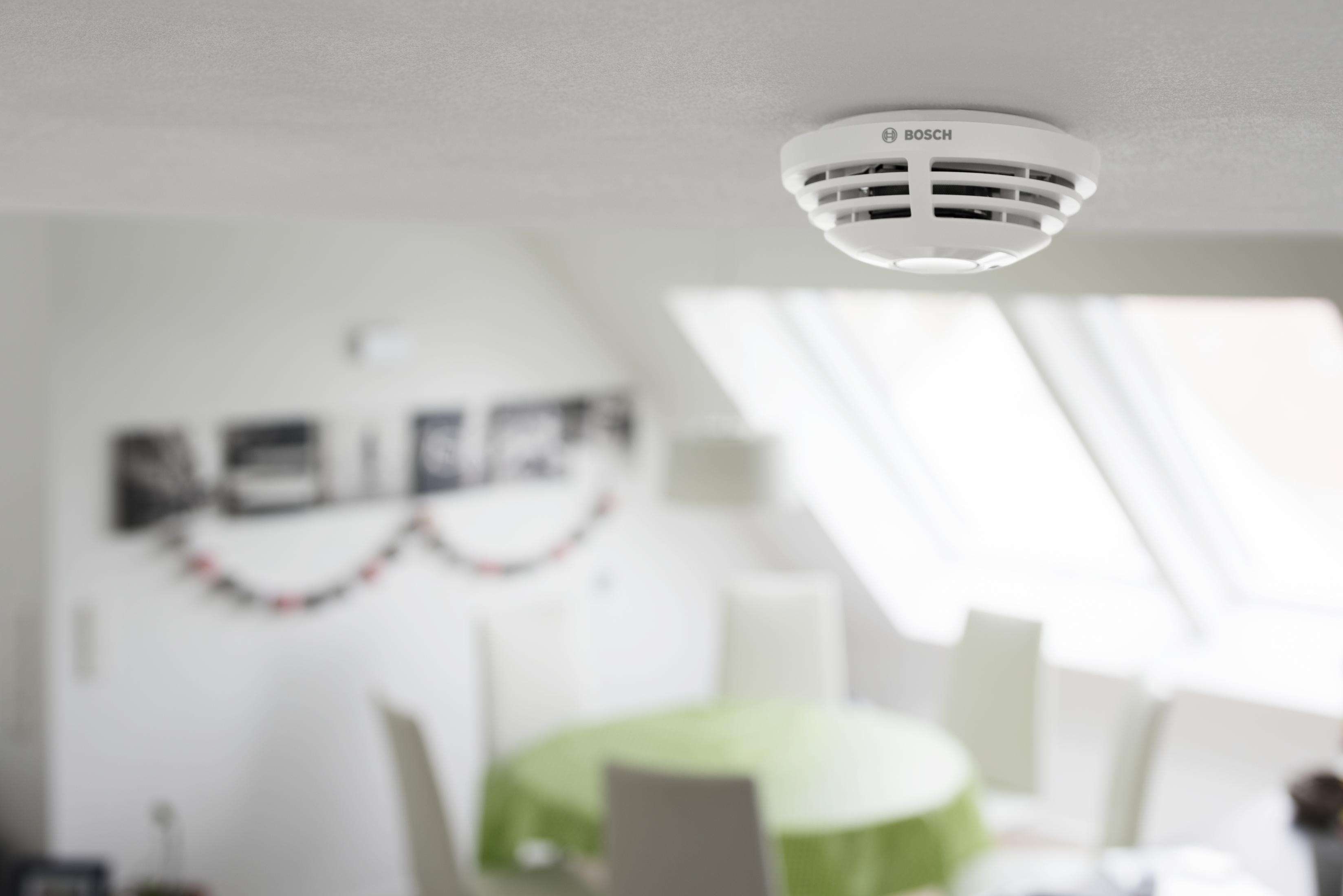 Weißer Rauchmelder an einer Decke. Verschwommener Hintergrund mit Esszimmer.