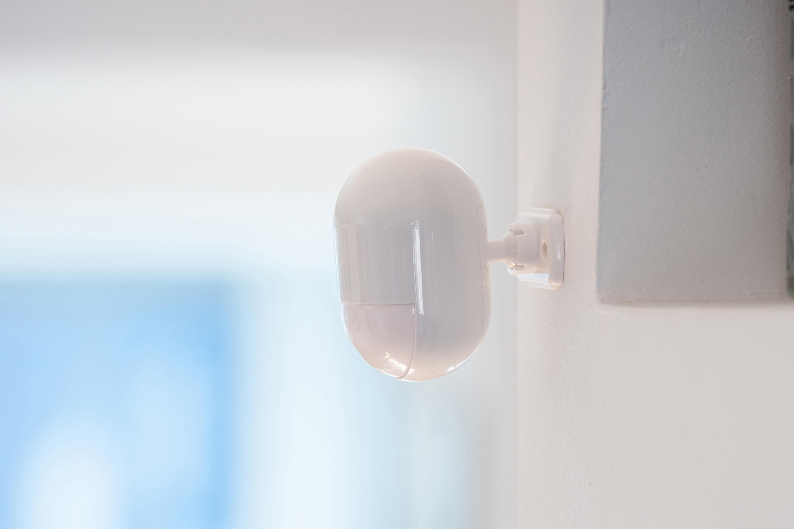 Biały, owalny czujnik bezpieczeństwa zamontowany na białej ścianie.