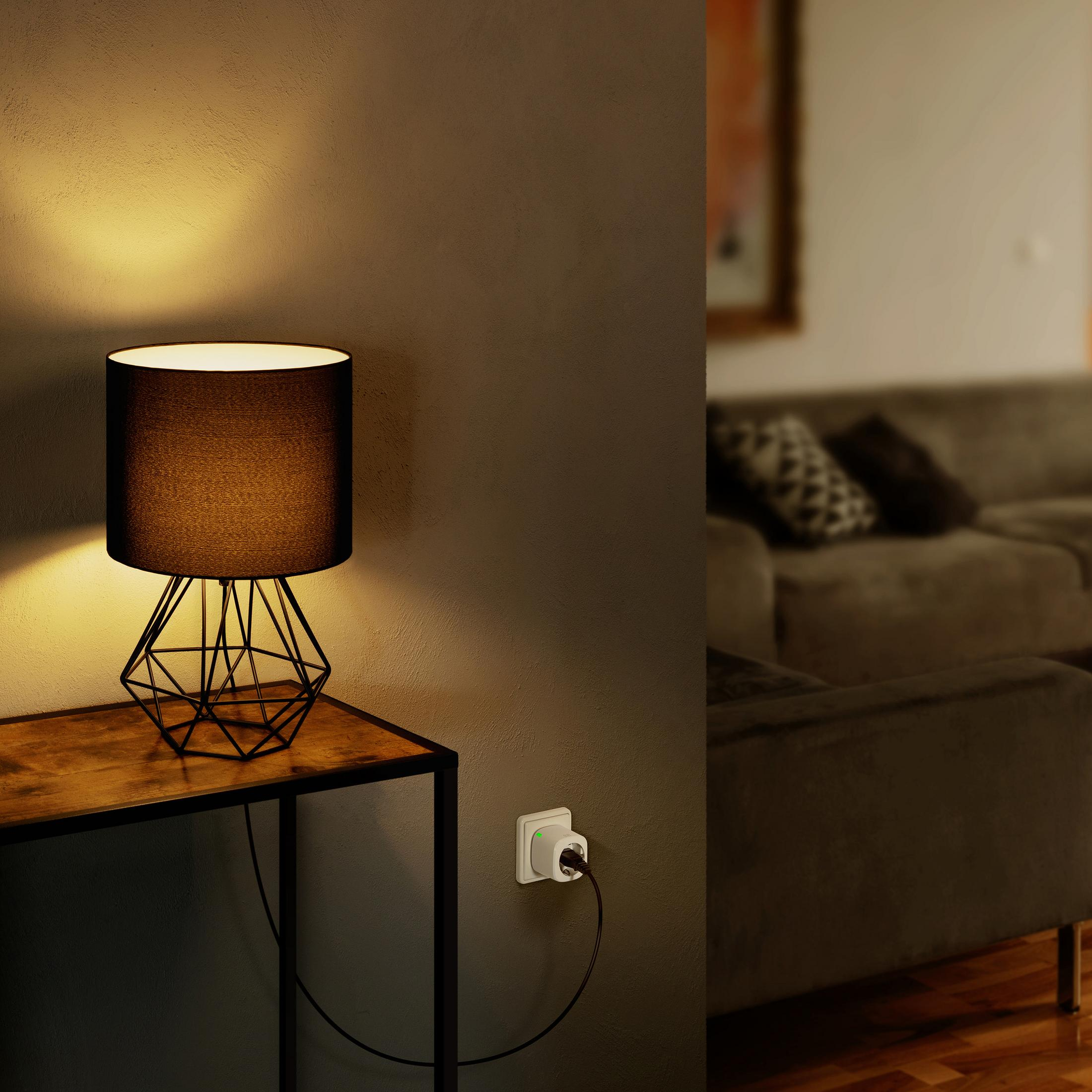 Tischlampe mit schwarzem Schirm. Smart Plug in der Steckdose. Sofa im Hintergrund.