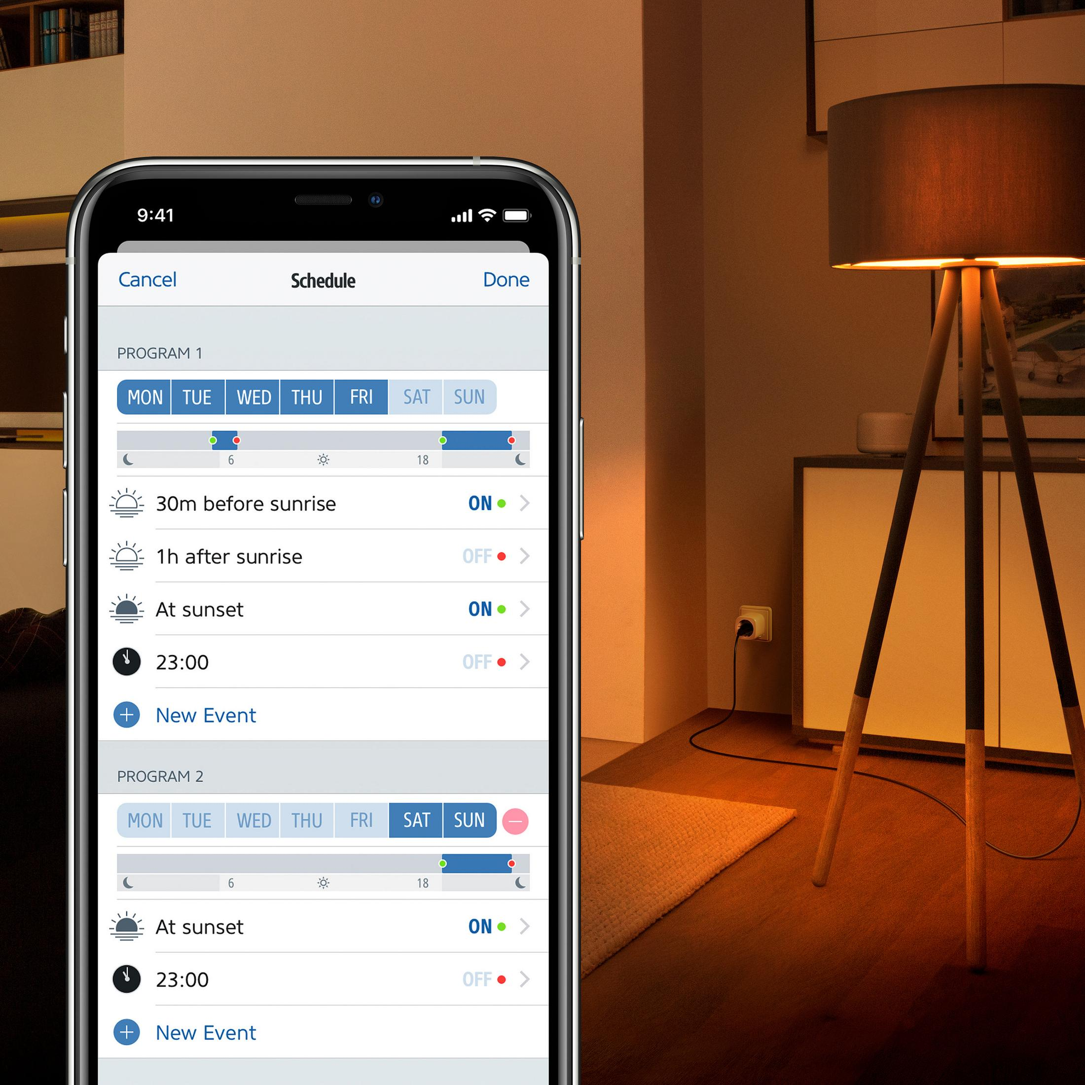 Ein Smartphone zeigt einen Zeitplan mit Ein/Aus-Zeiten an. Im Hintergrund sind eine Lampe und Möbel zu sehen.