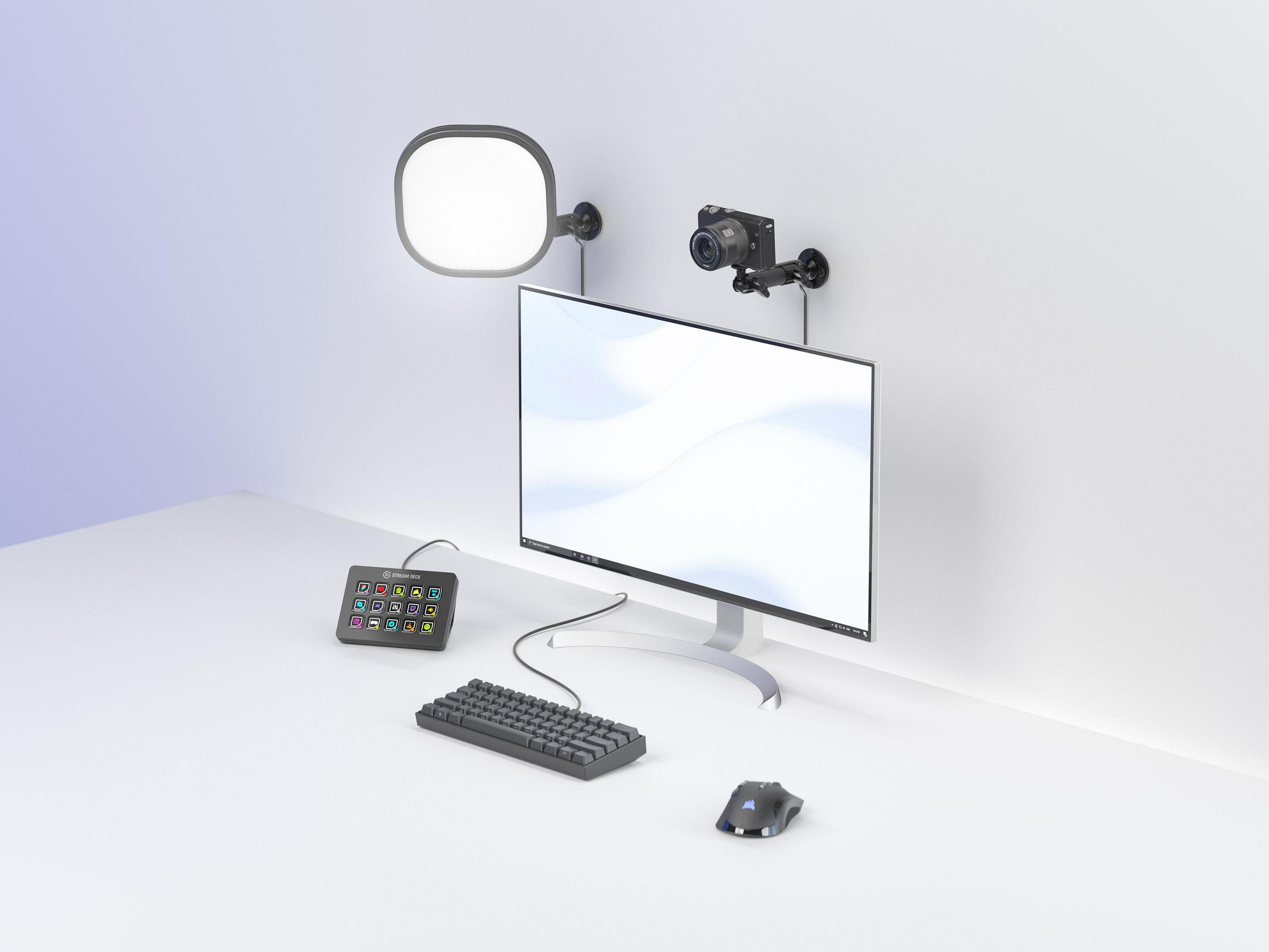 Schreibtisch mit Monitor, Kamera, Licht, Tastatur, Maus und schwarzem Bedienfeld. Weißer Wandhintergrund.