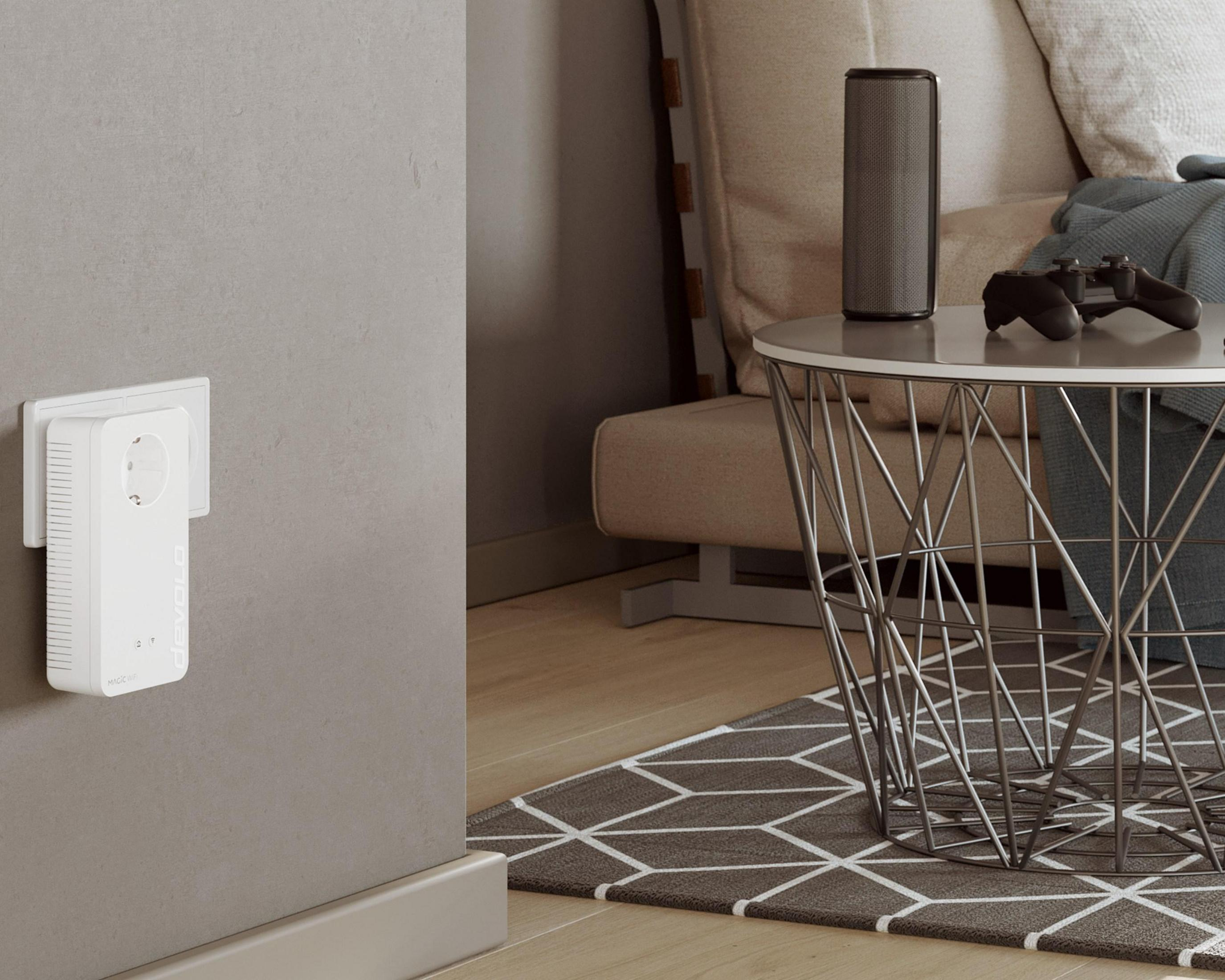 Biały zasilacz wpięty w szarą ścianę. Router i głośnik stoją na pobliskim stole.