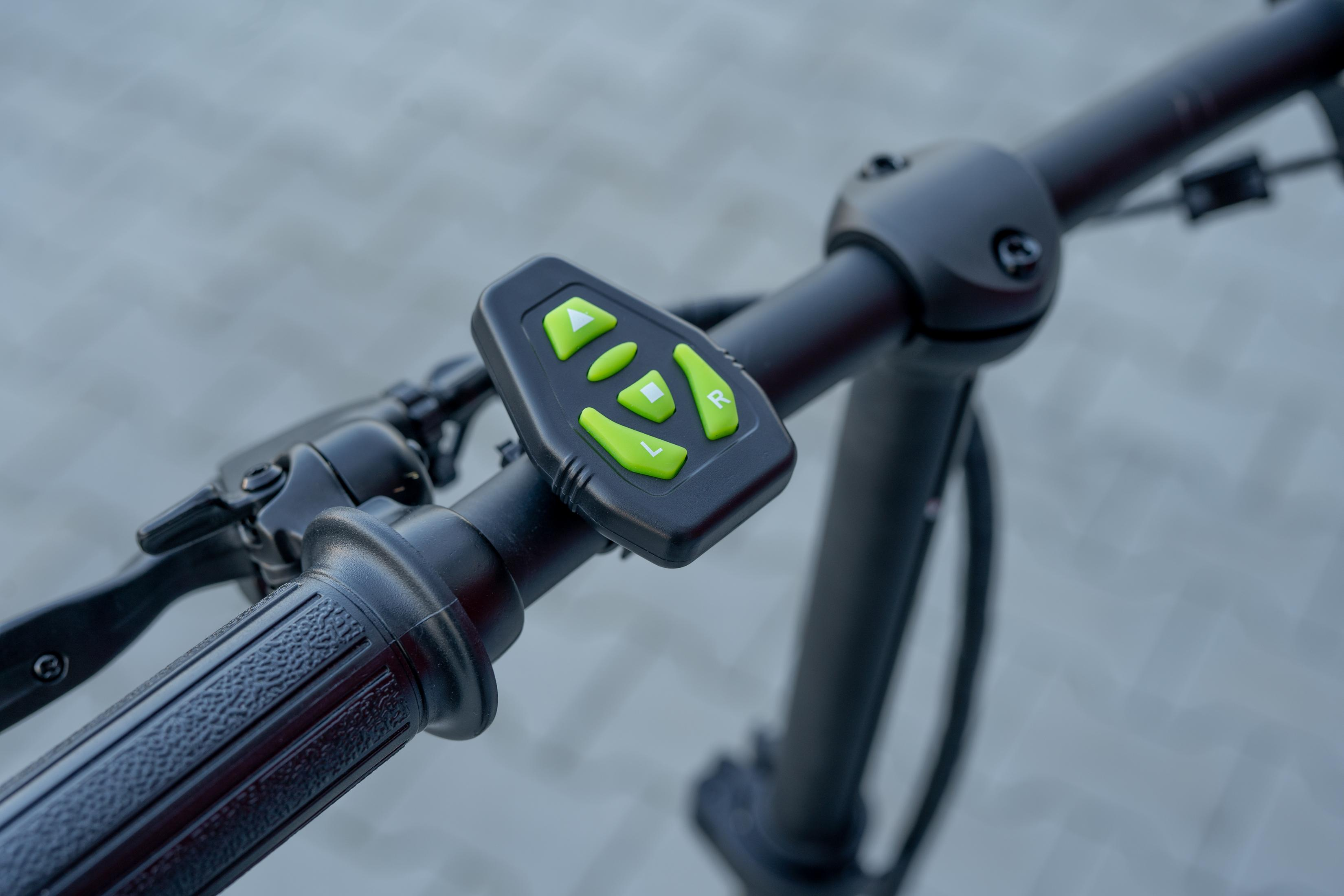 Nahaufnahme eines schwarzen Fahrradlenkers mit Bedienfeld und grünen Knöpfen.