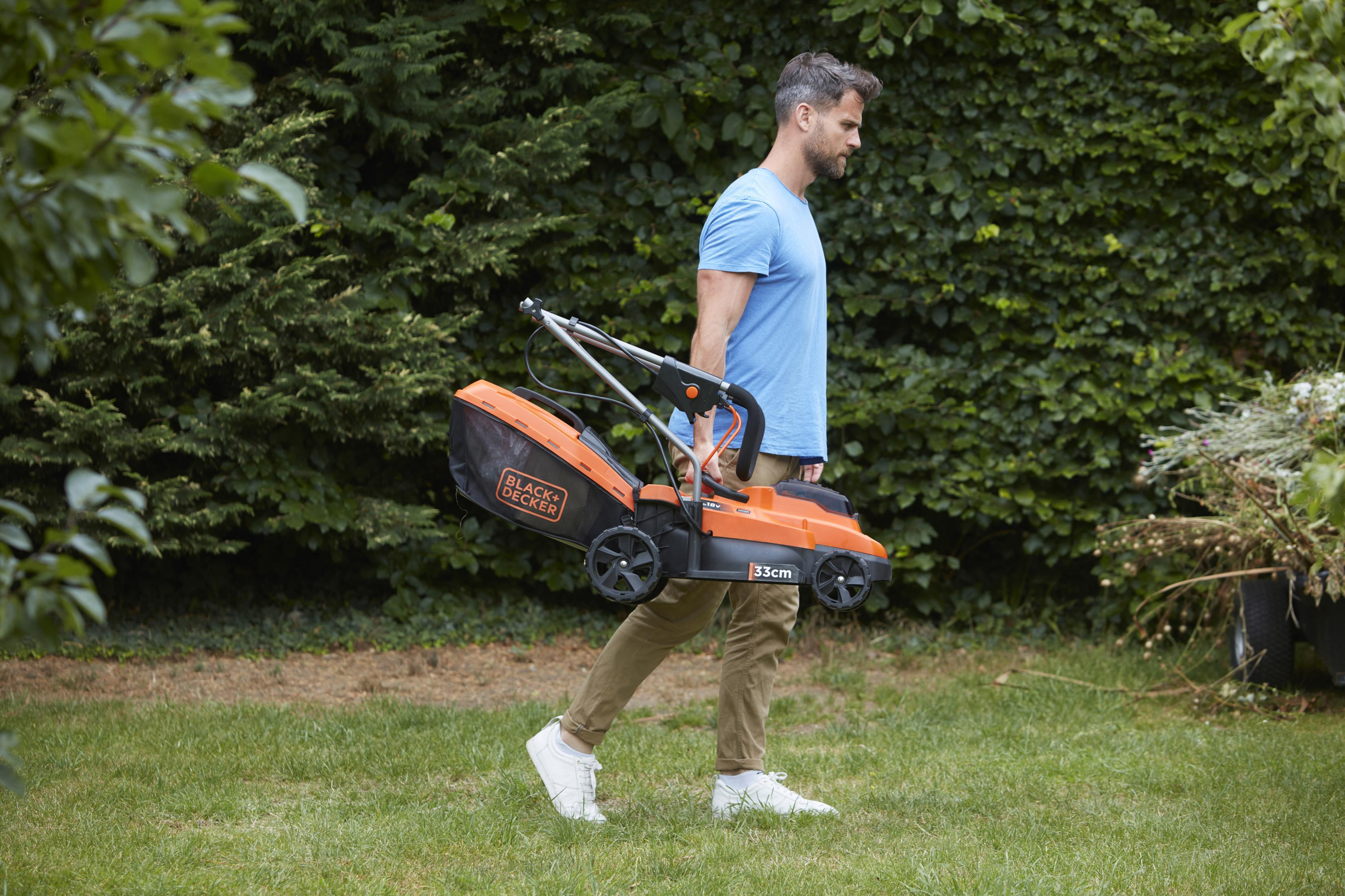 Ein Mann trägt einen schwarz-orangenen Rasenmäher über einen grünen Rasen.