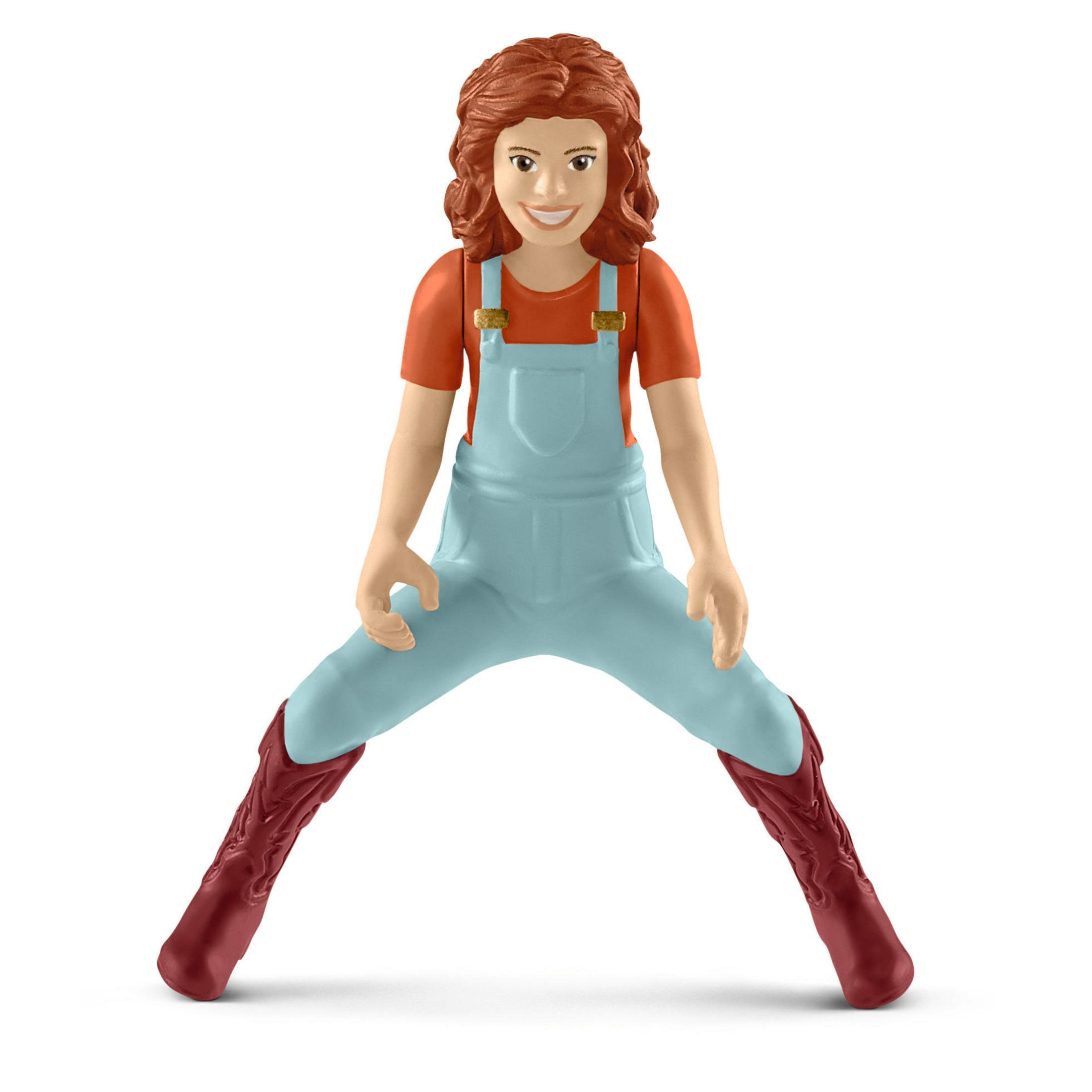 Une fille jouet en salopette bleue et bottes rouges. Elle sourit et se tient debout, les jambes écartées.