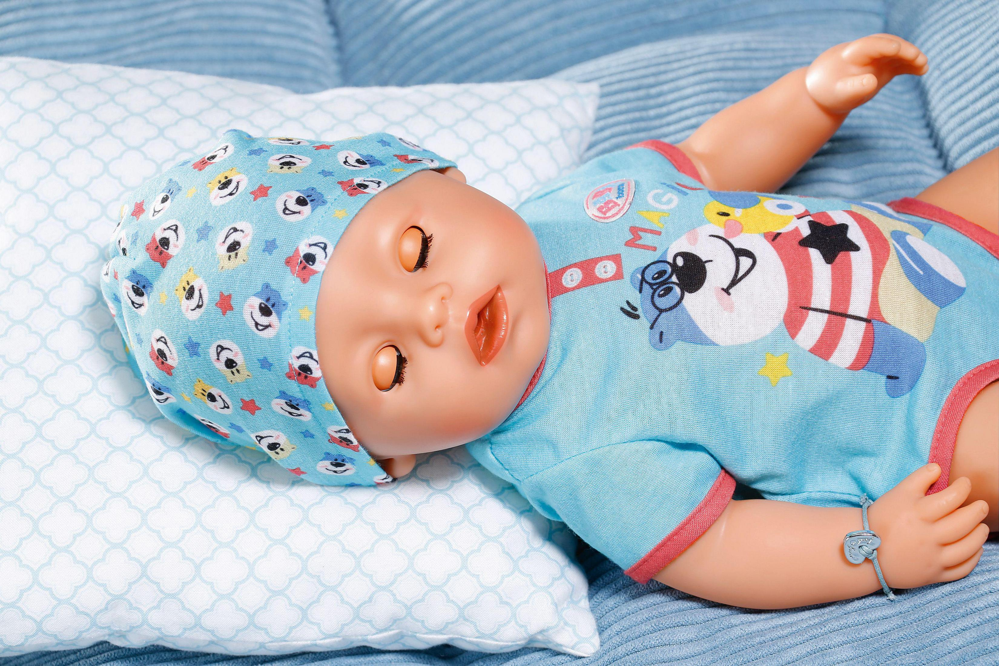 Babypuppe in blauem Strampler und Mütze, liegt auf einem Kissen. Der Hintergrund ist eine blaue Oberfläche.