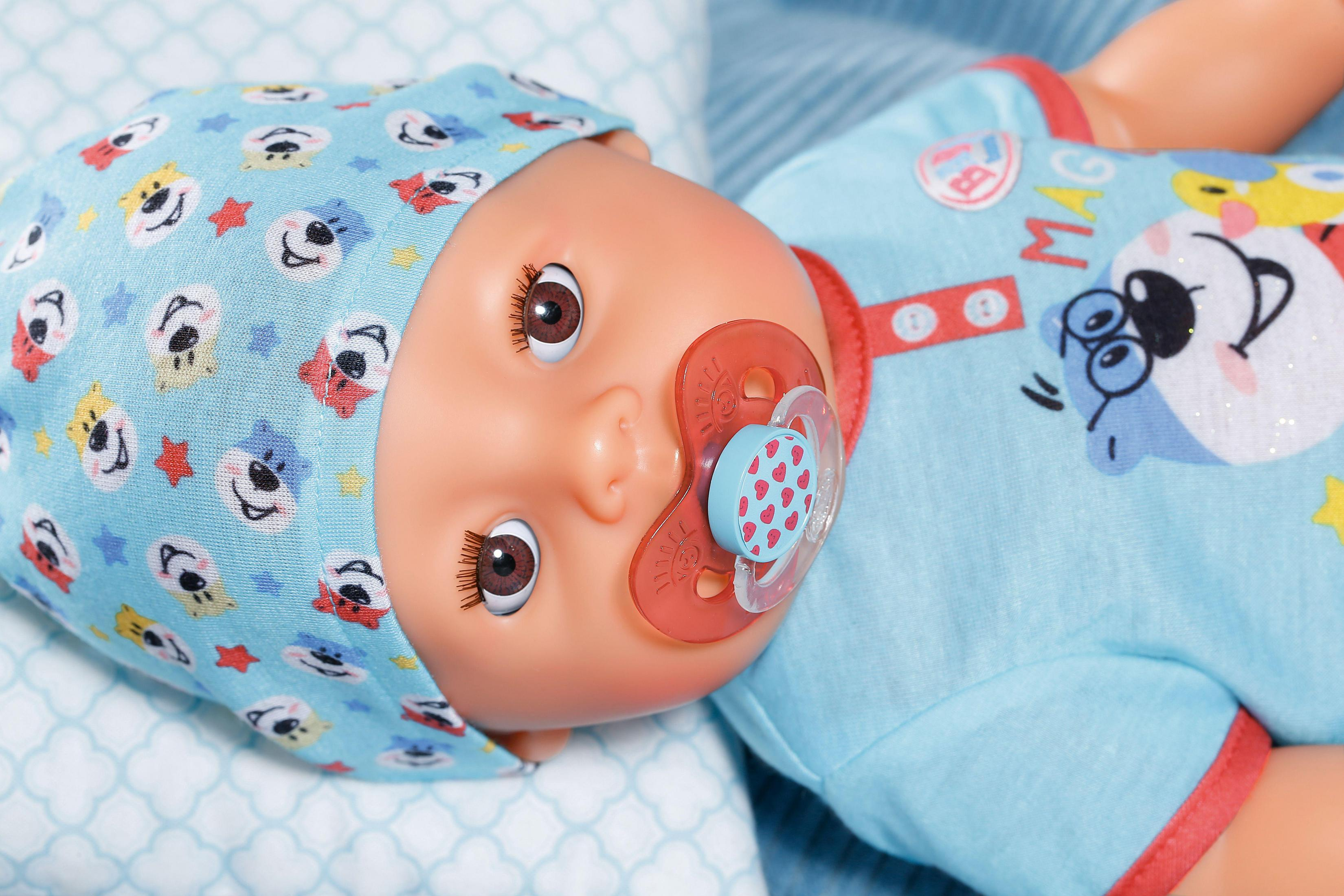 Babypuppe mit blauer Mütze, Schnuller und blauem Outfit. Liegend auf blauer Oberfläche.