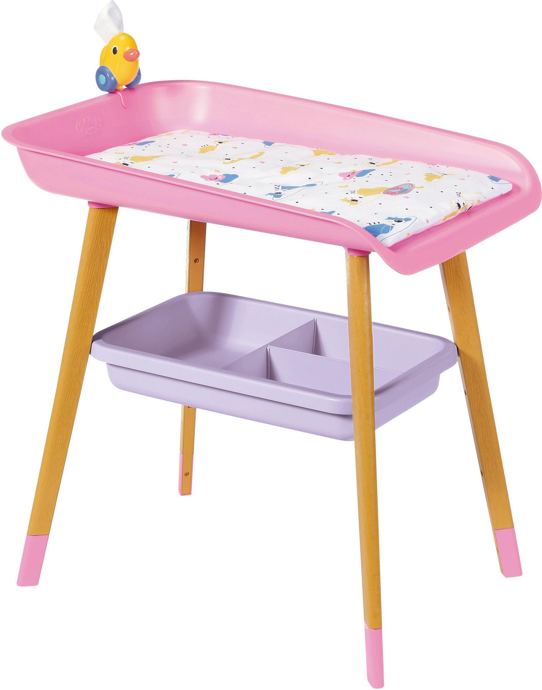 Cambiador rosa para bebés con patas de madera y estante de almacenamiento.