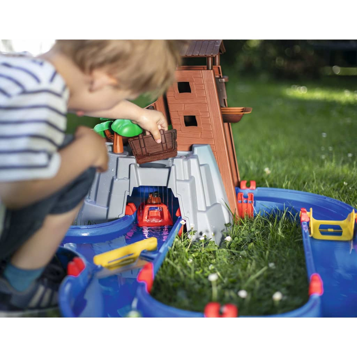 Ein Kind spielt mit einem Wasserspielzeug-Set im Garten.