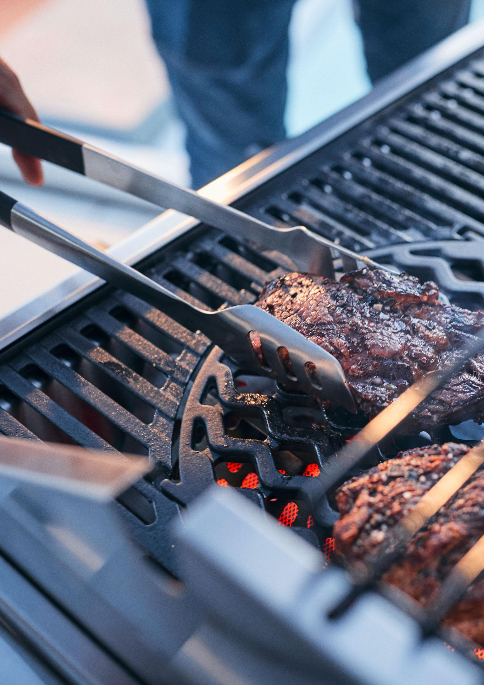 Nahaufnahme des Grillens mit Zangen, die einen Steak auf einem heißen Grill halten.