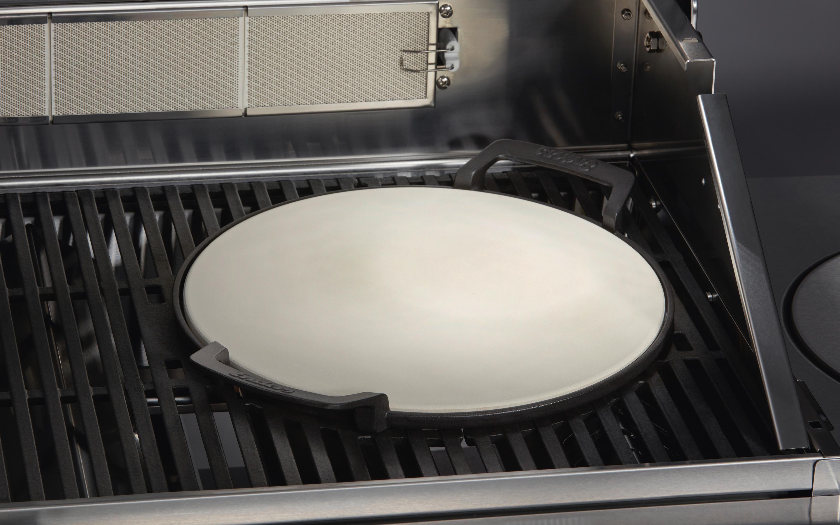 Ein Pizzastein auf einem Grill mit dunklem Hintergrund.